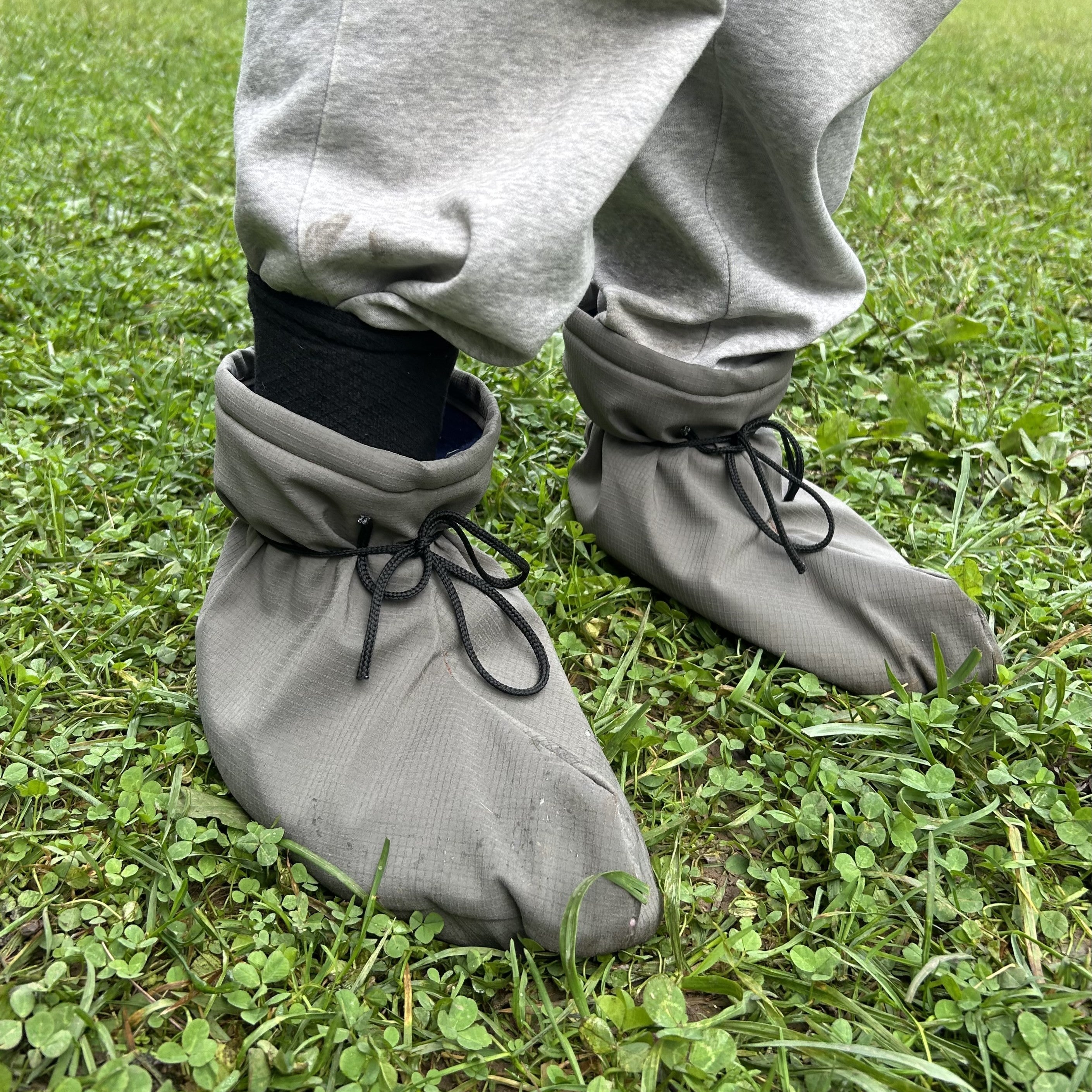 Outside standing on green grass wearing light grey sweatbands and a greenish brown pair of booties.