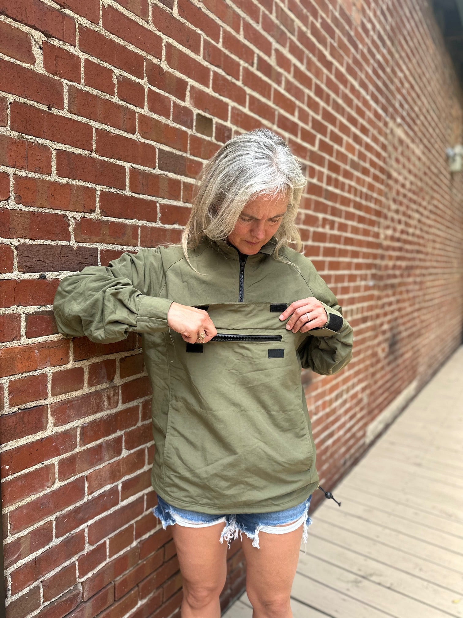 Woman wearing a green anorak against a brick wall