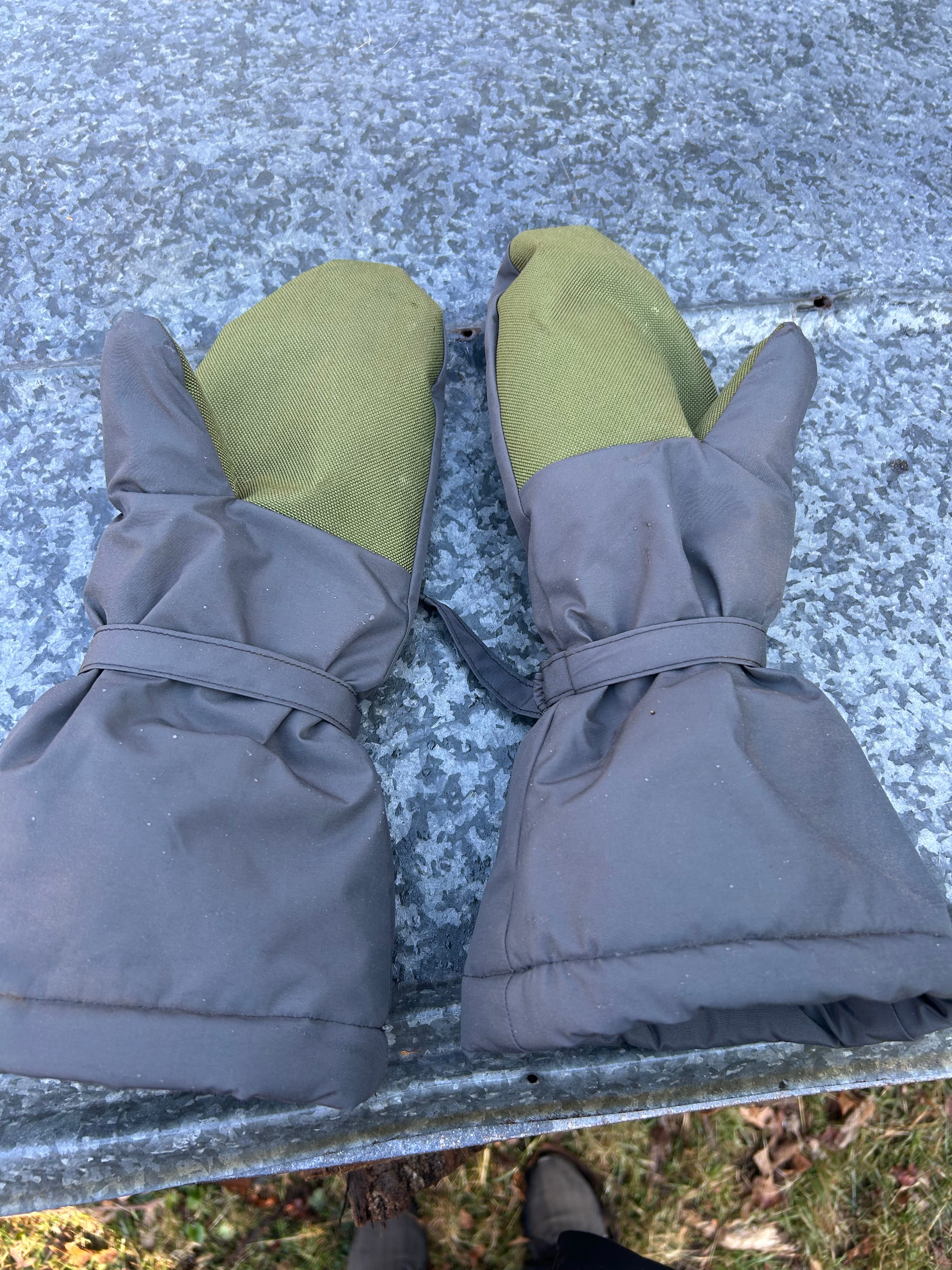 Pair of grey mittens with green hand grips on a piece of sheet metal outside.