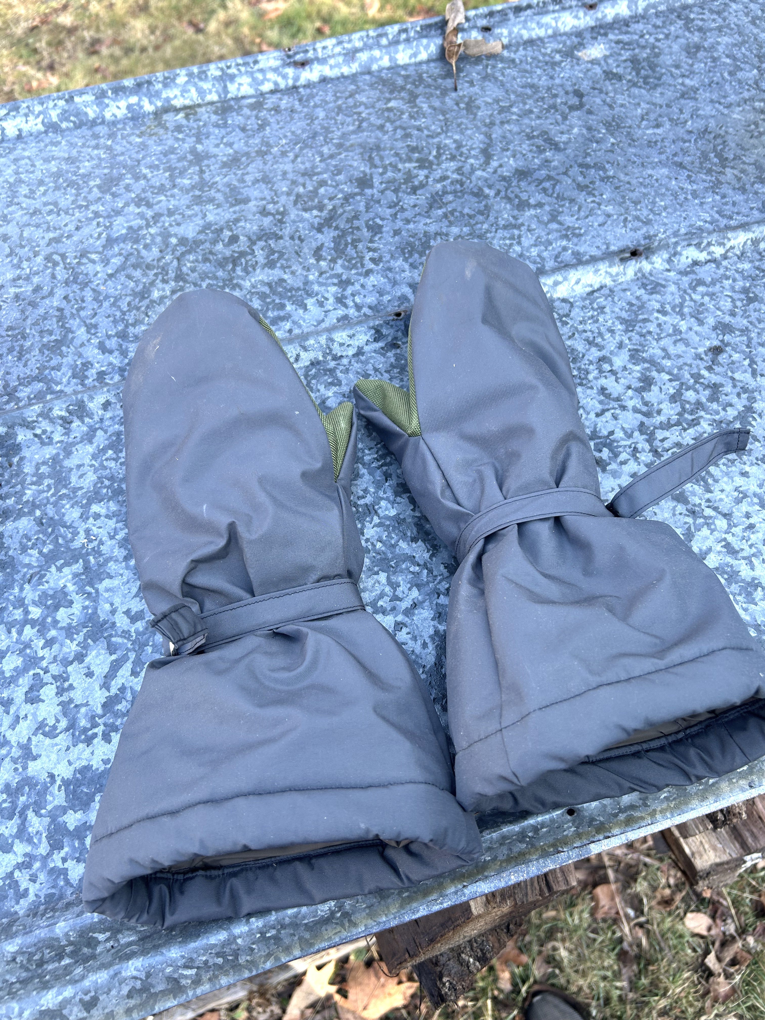 Pair of grey mittens on a piece of sheet metal outside.
