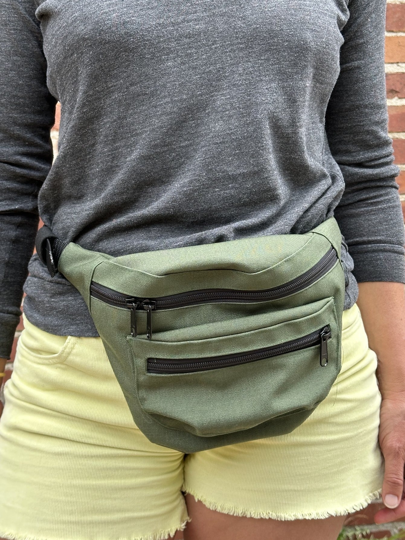 close up of woman wearing an olive fanny pack, yellow shorts, and grey shirt