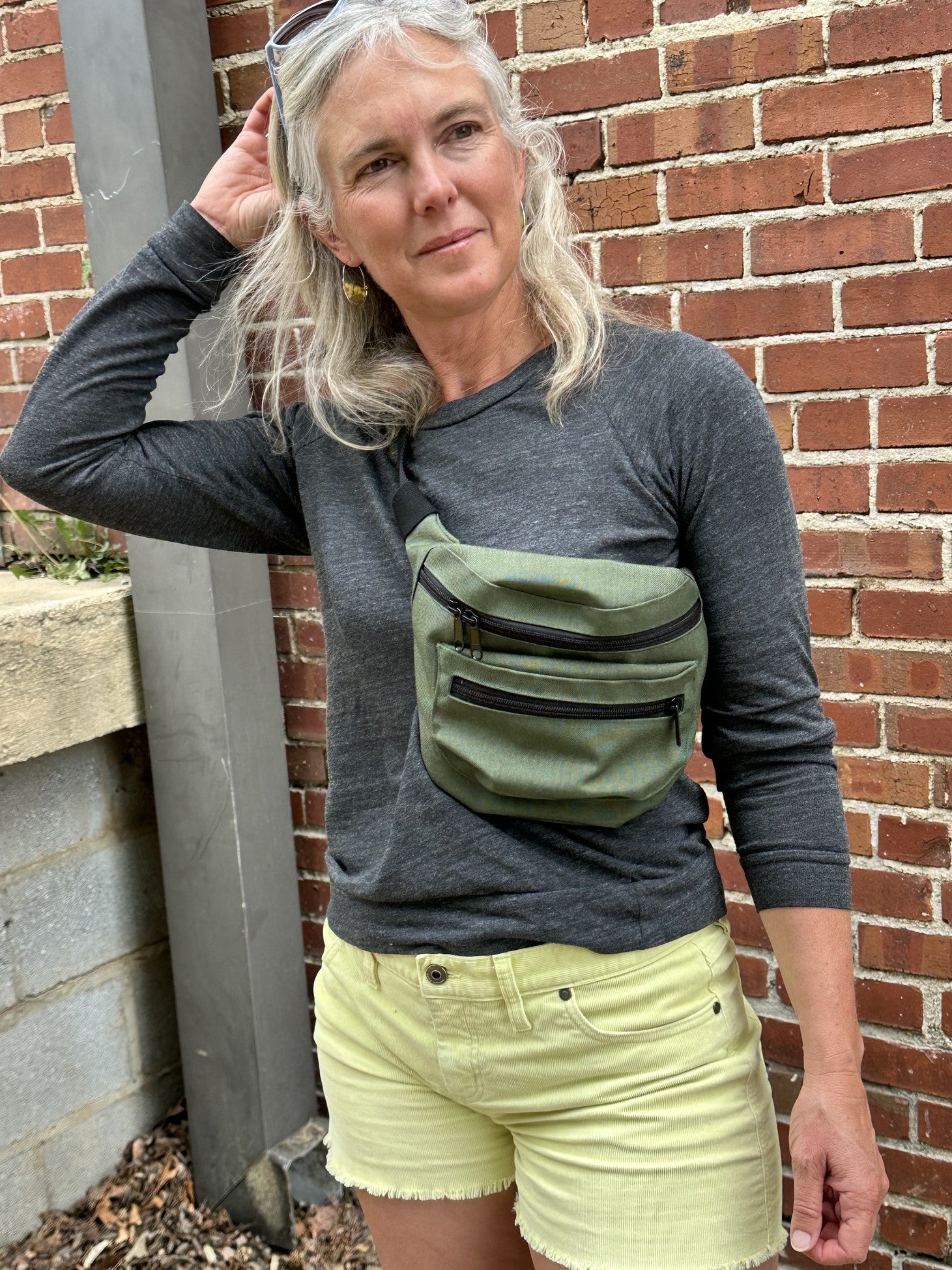 Woman wearing a green fanny pack against a brick wall.