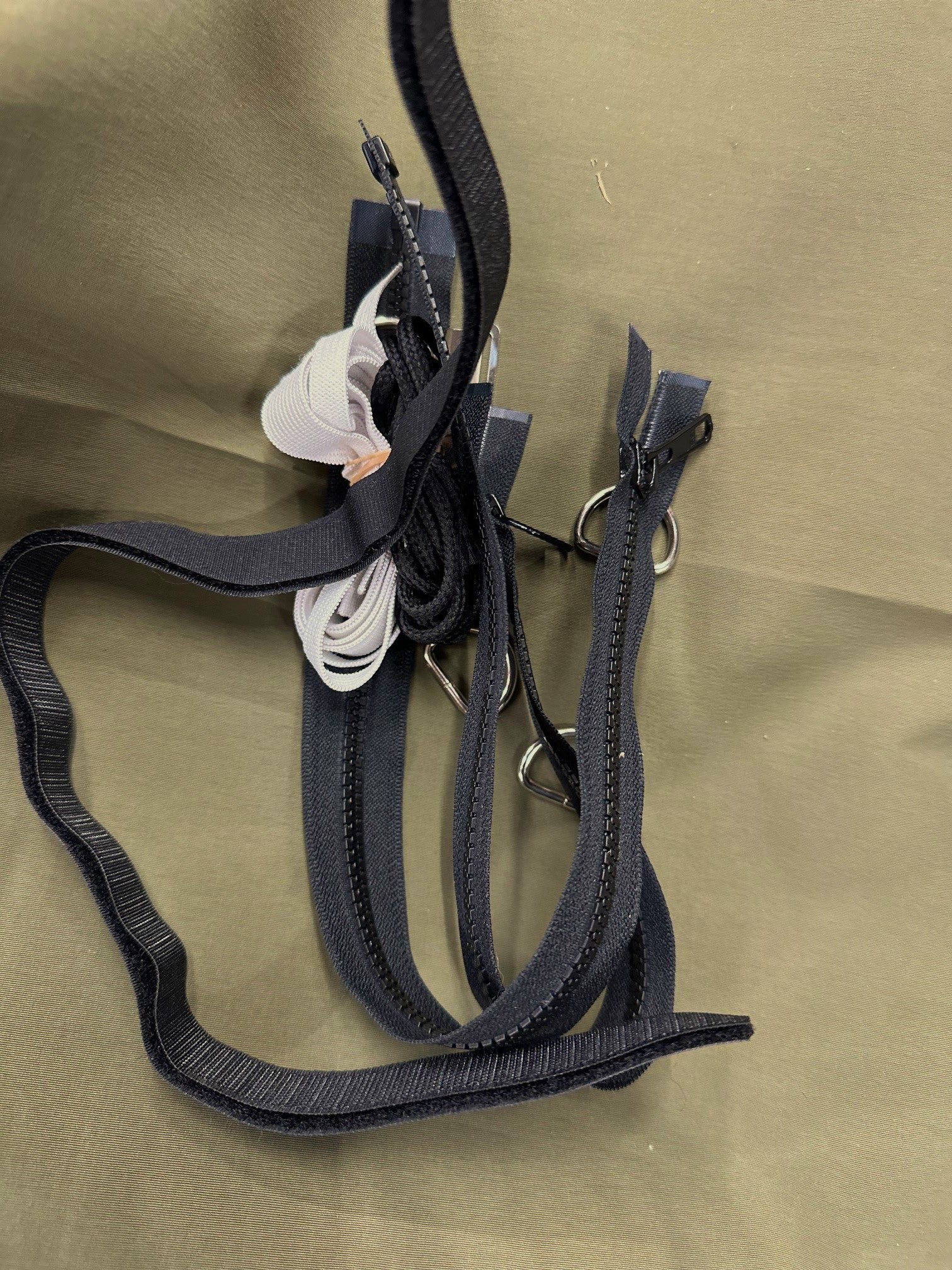 two zippers, velcro, cording, Drings, and white elastic with olive fabric