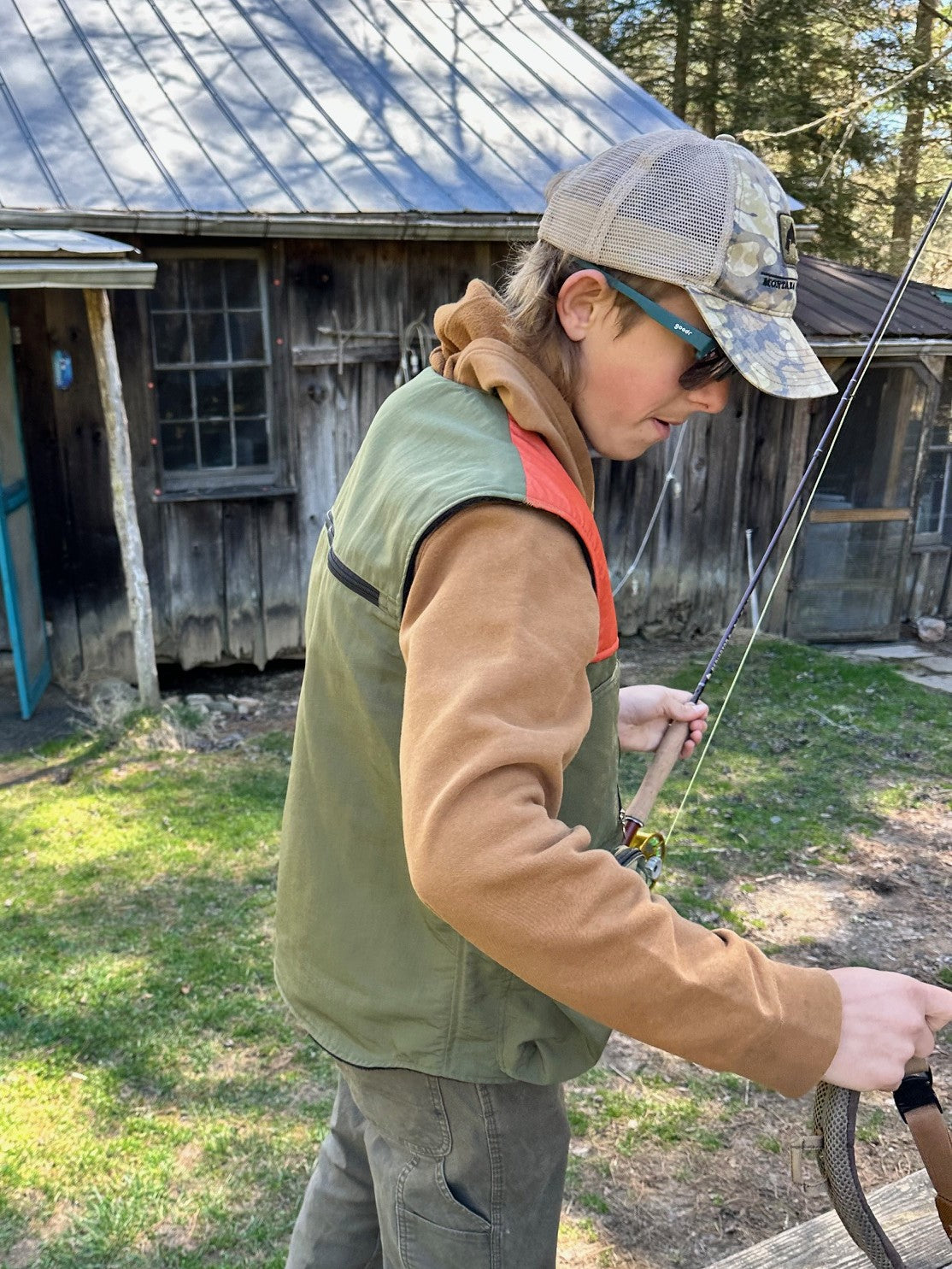 Person holding a fishing rod outdoors near a wooden building