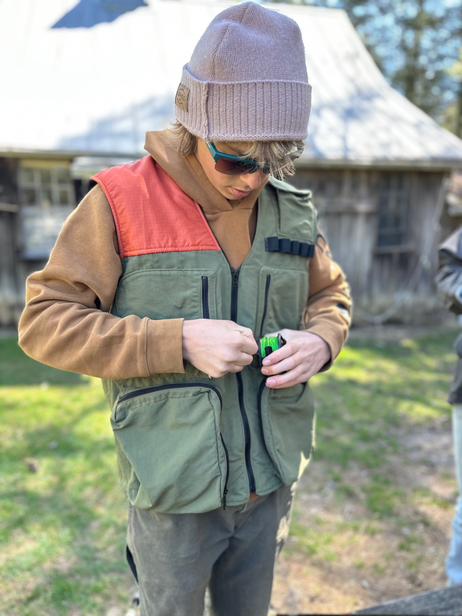 Person wearing a green vest with a red interior, brown jacket, and gray beanie outdoors.