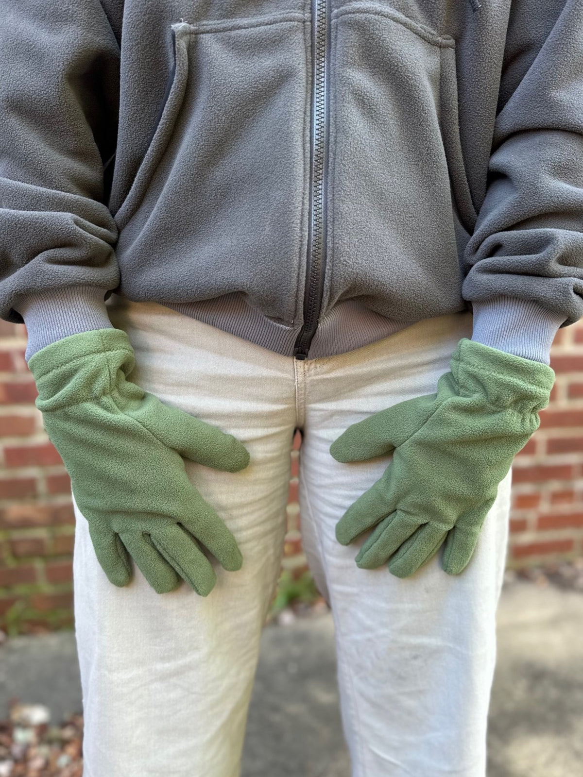 close up of a person with green fleece gloves, grey sweatshirt, and tan pants