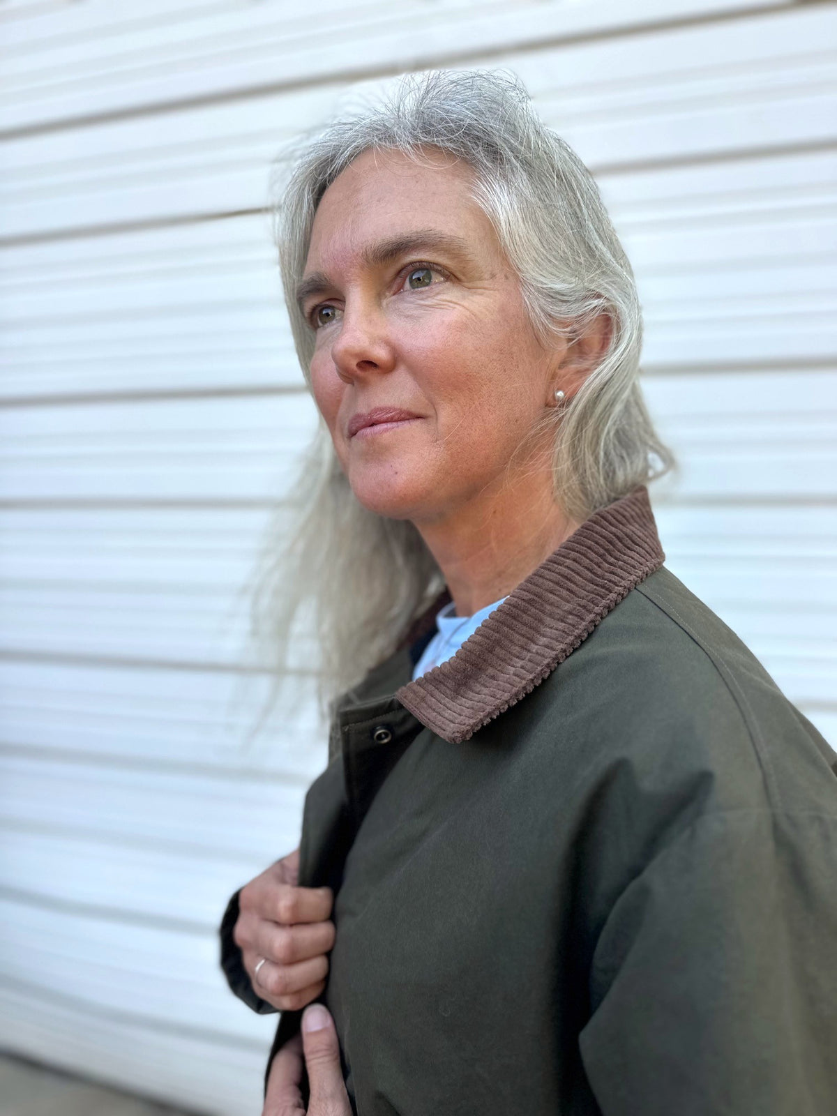 Close up of Woman standing in front of a white garage door wearing an olive barn jacket with a brown corduroy collar