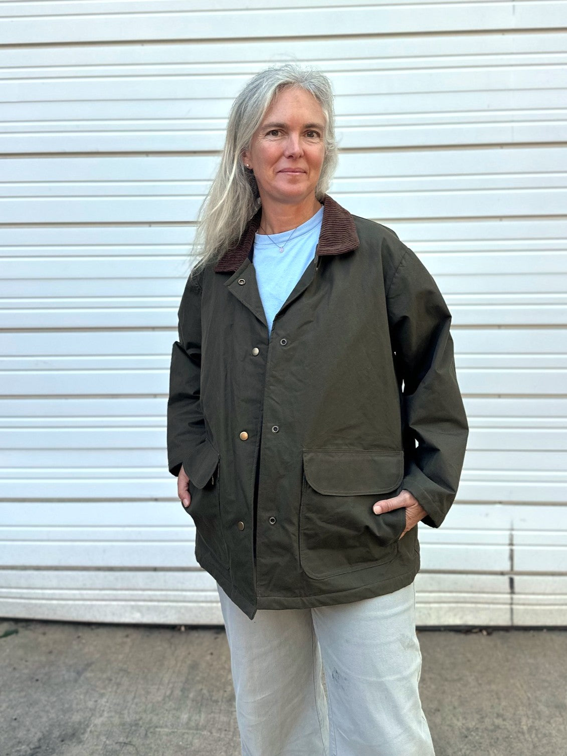 Woman standing in front of a white garage door wearing tan pants and an olive barn jacket