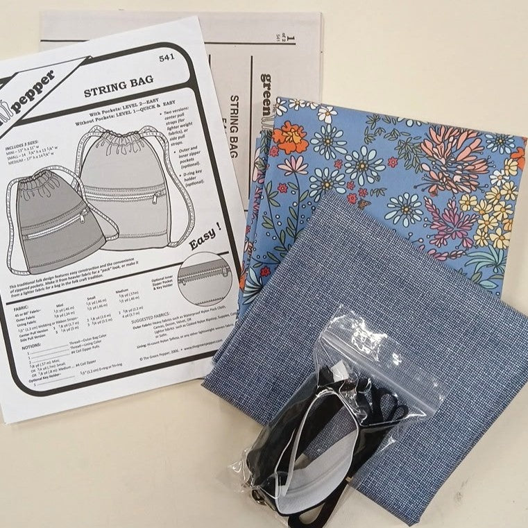 Craft kit with fabric, patterned paper, and string bag instructions on a light surface.