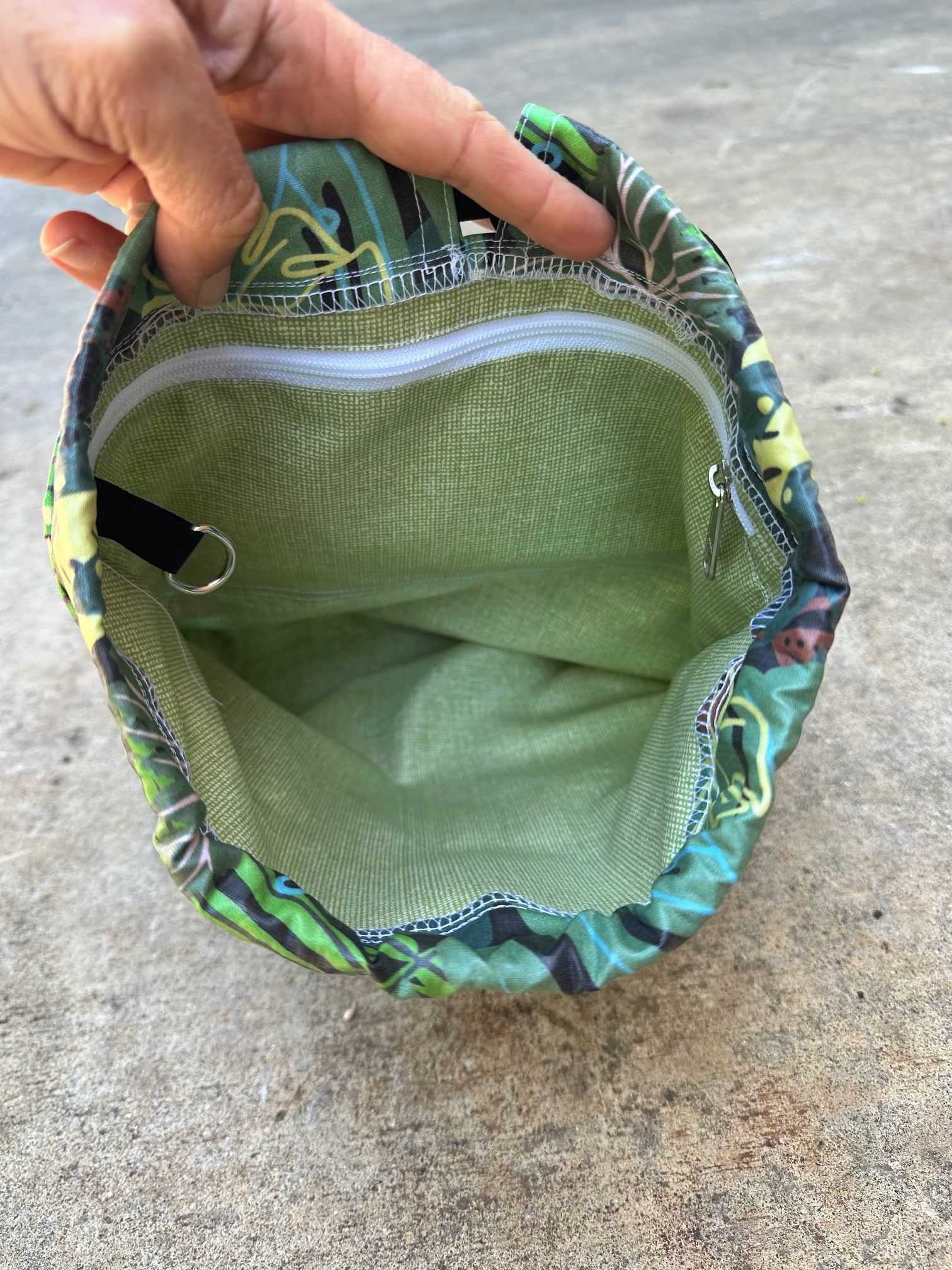 Hand holding a green fabric pouch open with floral pattern on a concrete surface