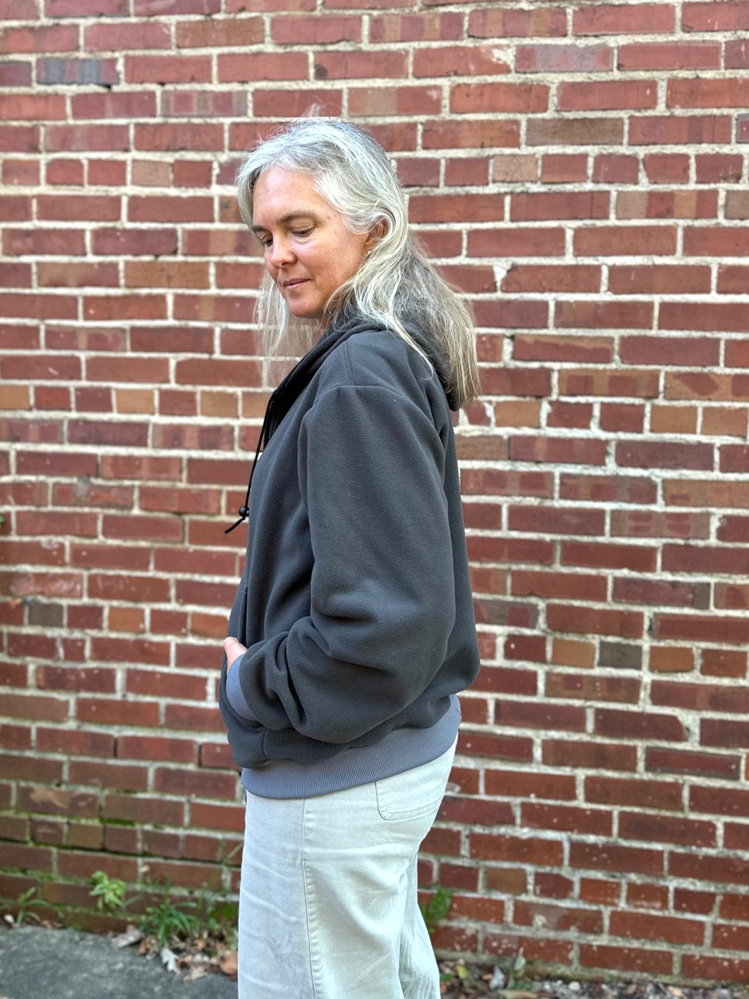 woman wearing a grey fleece zip up sweatshirt outside by a brick wall