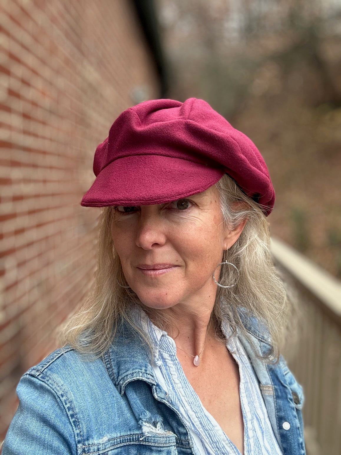 Woman wearing a red beret and denim jacket standing against a brick wall.
