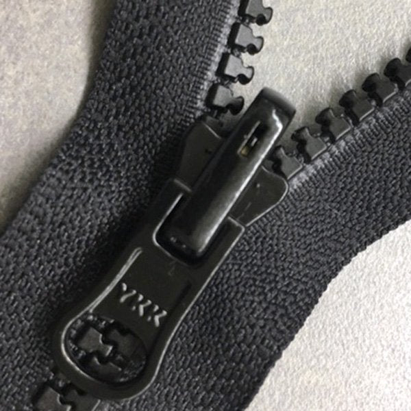 Close-up of a black zipper with a visible brand logo on a neutral background