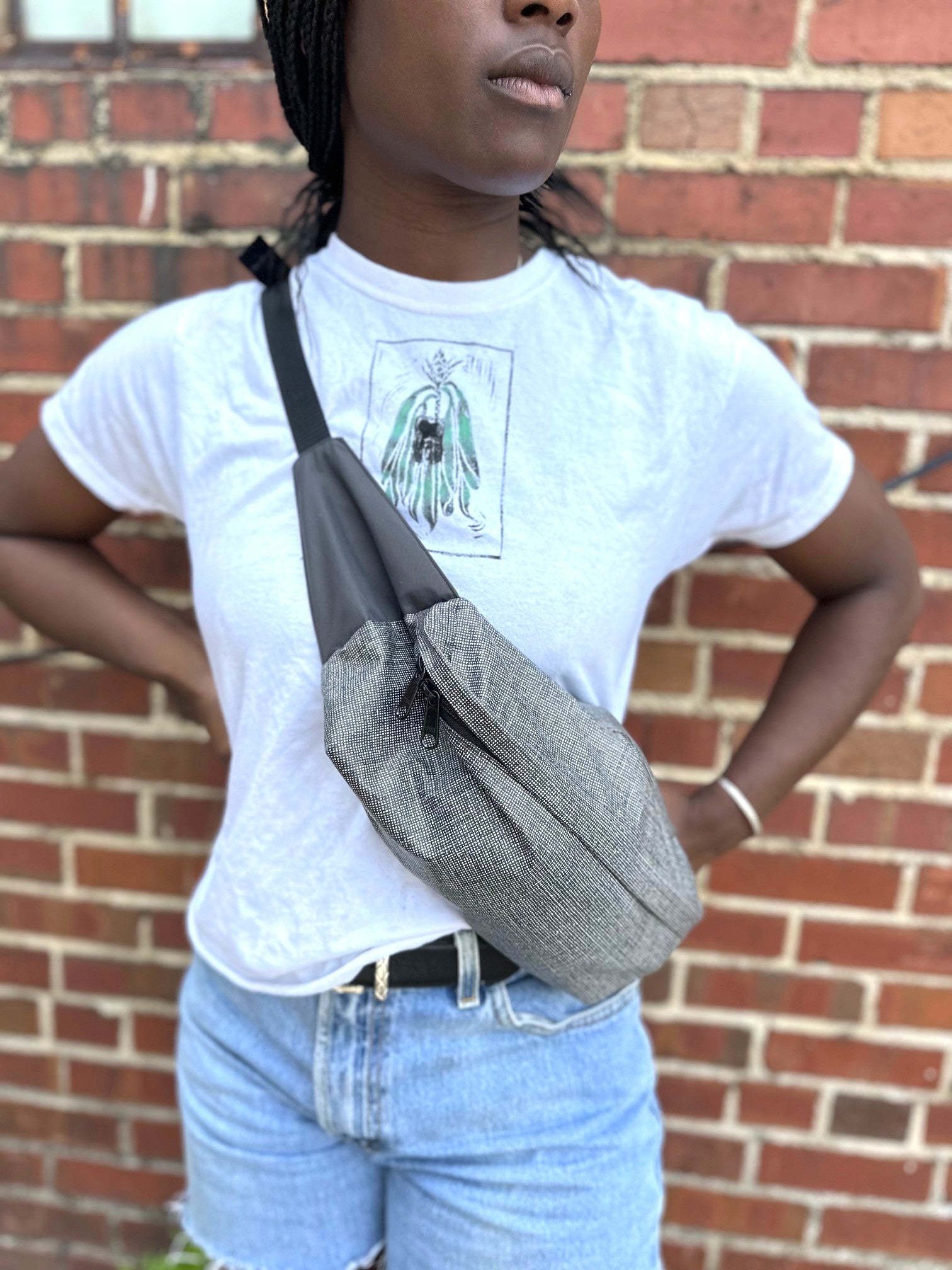 Person wearing a gray crossbody bag in front of a brick wall