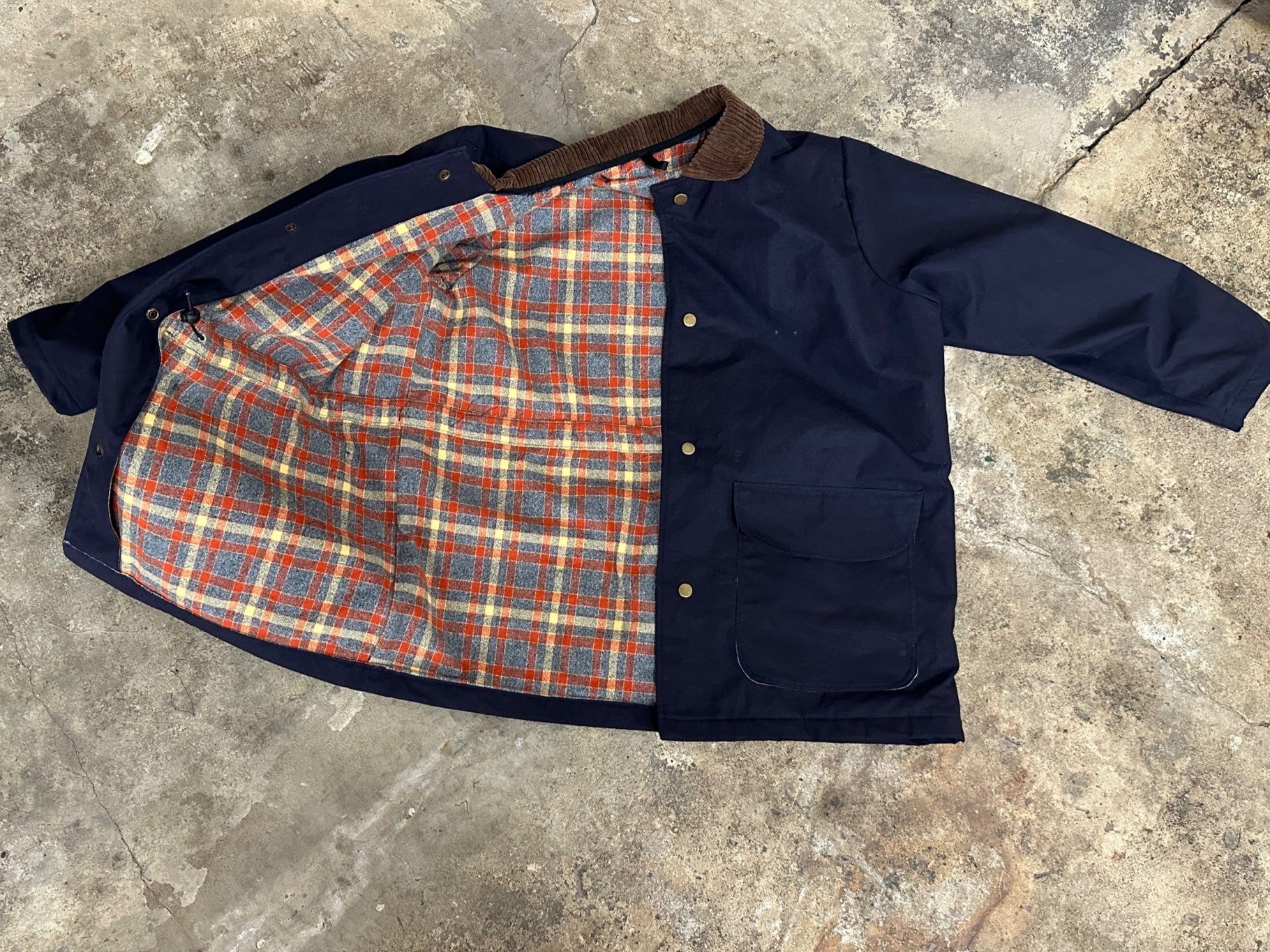 Navy jacket with plaid lining on a concrete floor