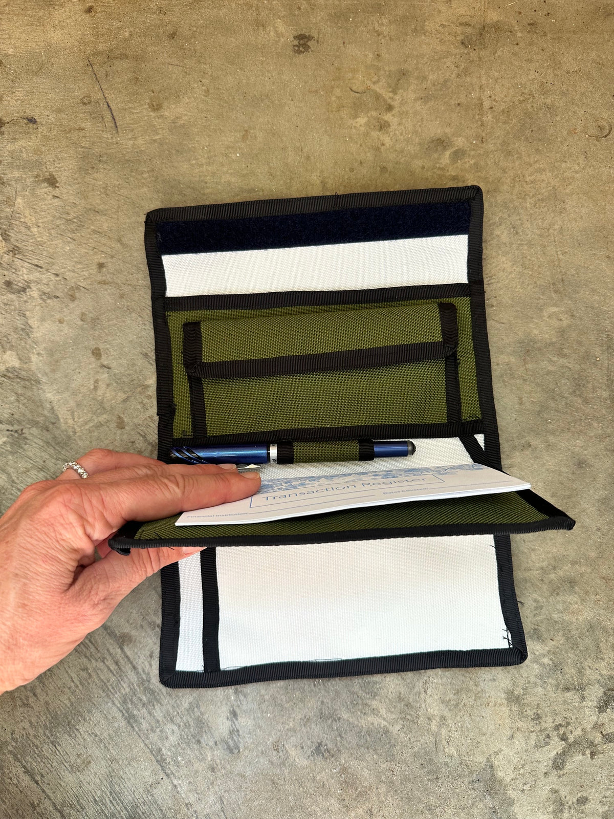 green checkbook wallet with black trim opened up with a pen on a concrete floor