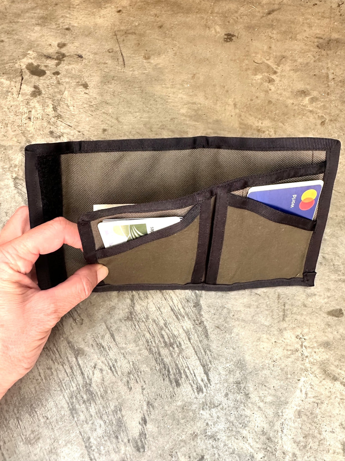Small olive colored wallet with black trim opened up on a concrete floor