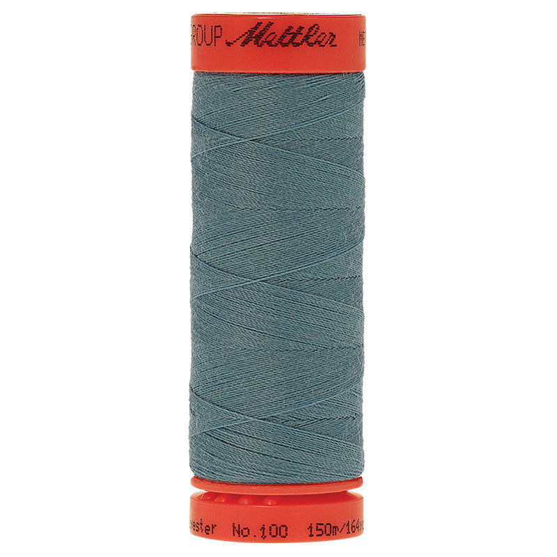 A spool of sewing thread wound on a red spool, featuring a dusty slate blue-gray thread body with red plastic end caps. The brand name 'Mettler' is printed in black on the top red cap.
