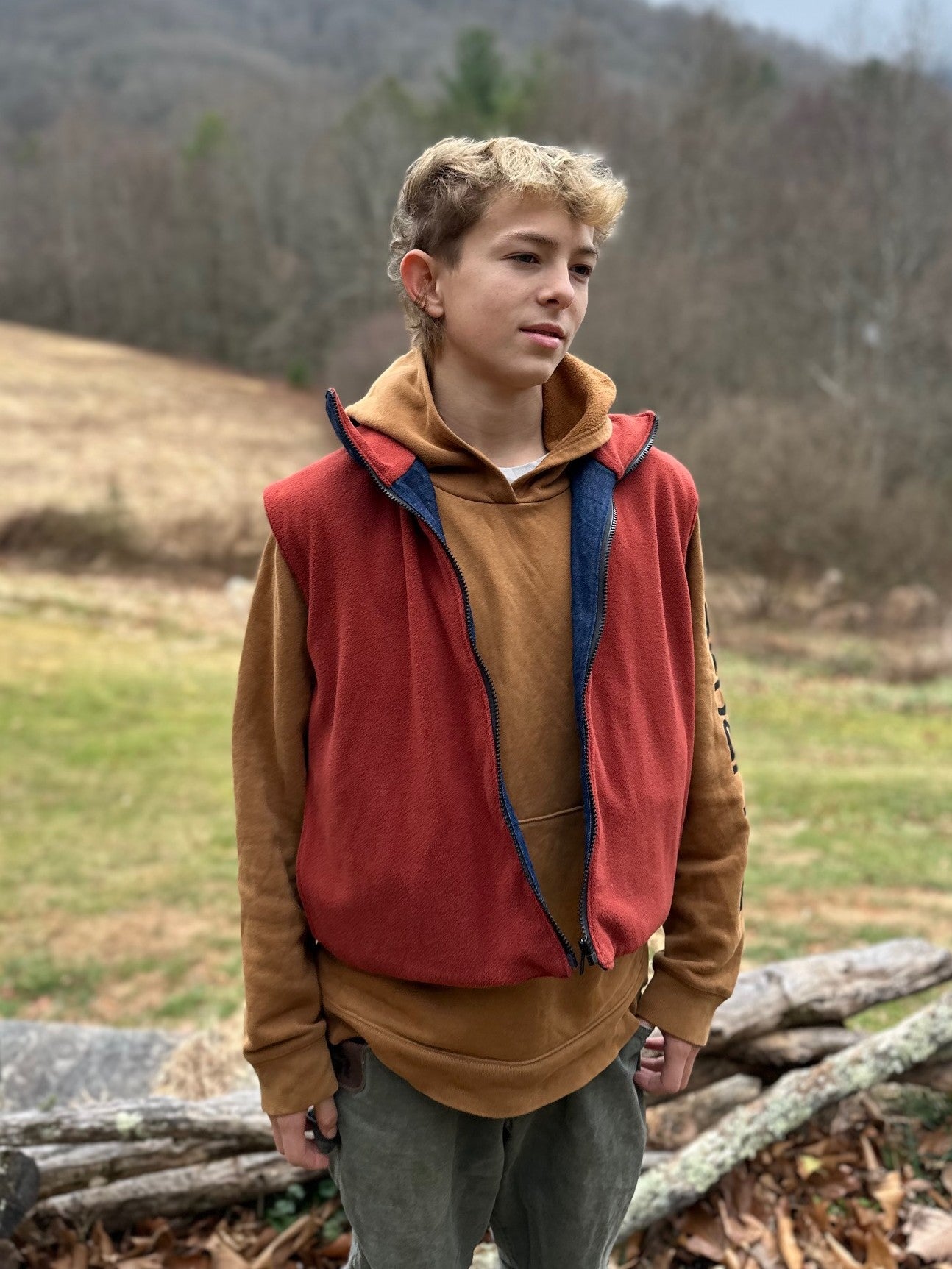 Person wearing a red vest over a brown shirt in a natural setting with trees and grass.