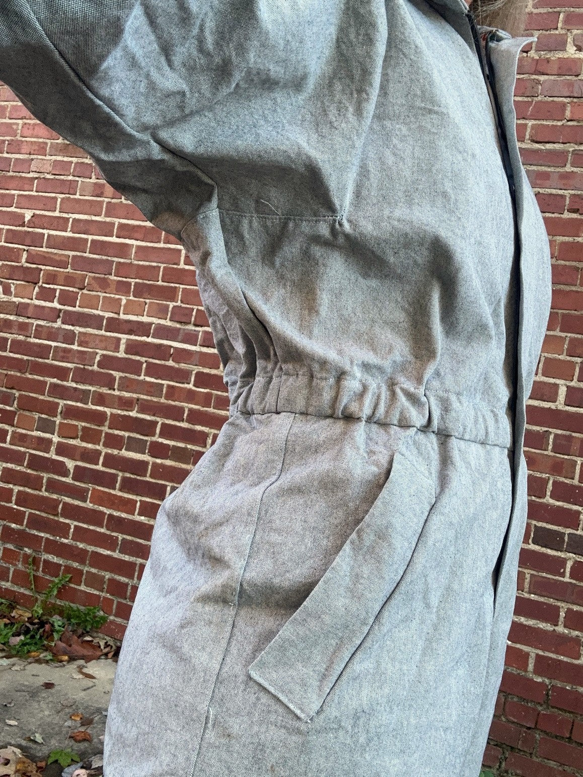 Light gray jumpsuit against a brick wall - close up of underarm