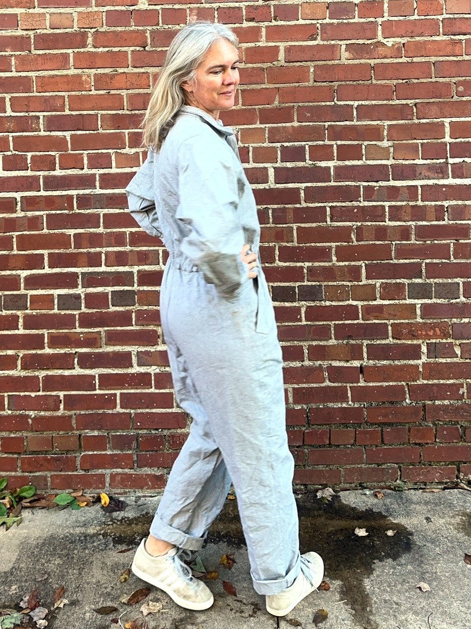 Person wearing a light blue jumpsuit standing against a brick wall.