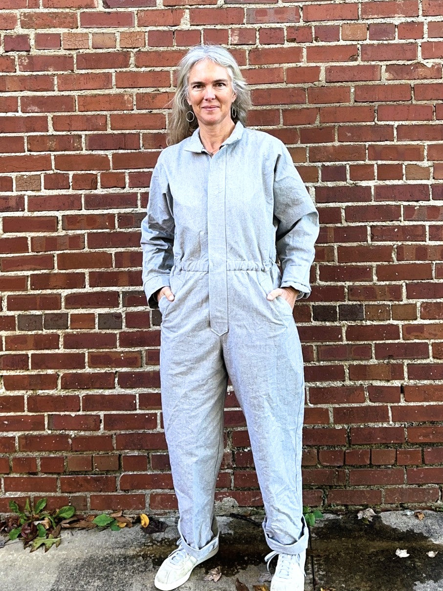 Person wearing a gray jumpsuit standing against a brick wall.