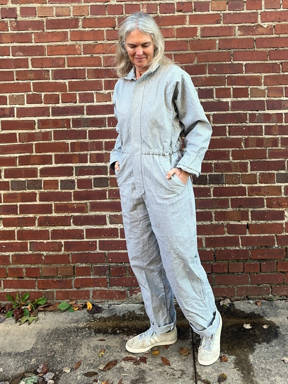 Person wearing a gray jumpsuit standing against a brick wall.