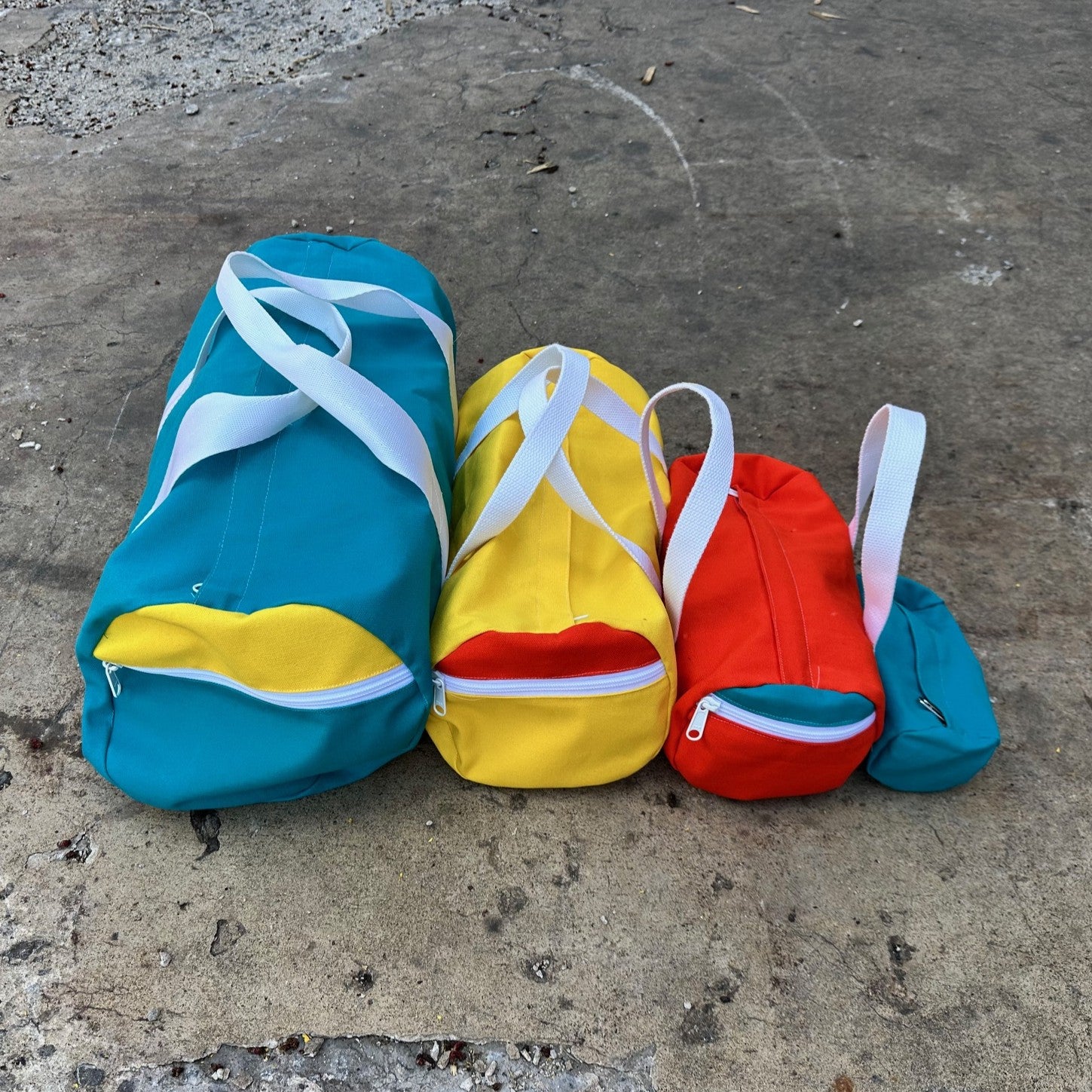 Four colorful bags in blue, yellow, red, and green on a concrete surface.