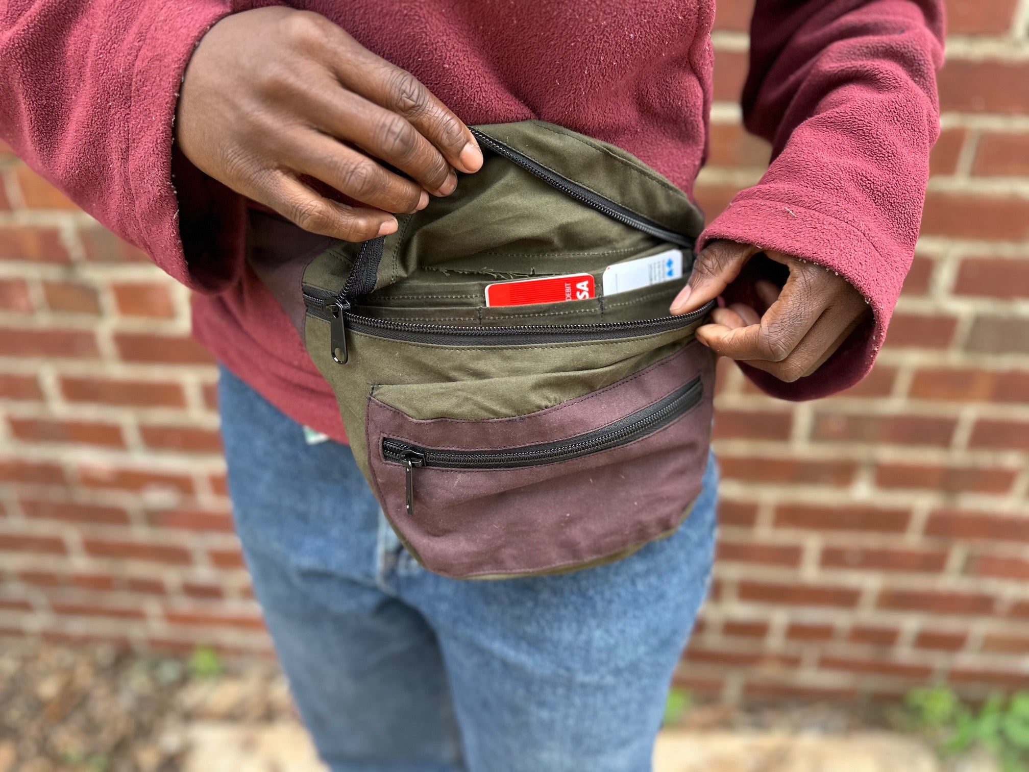 Person holding a green waist bag with a brick wall background