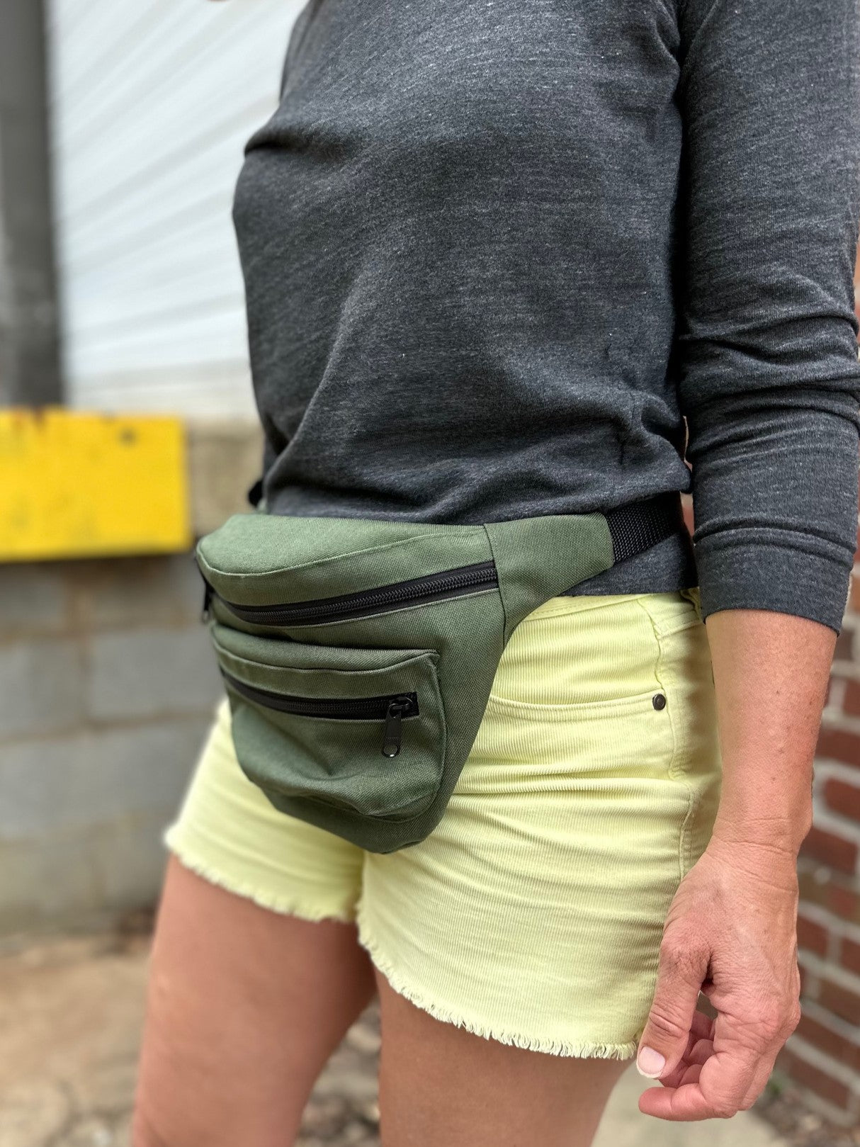 Person wearing a green fanny pack with a gray long-sleeve shirt and light yellow shorts.