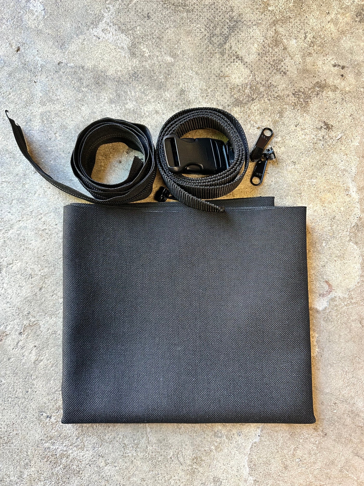 Black folded fabric with a straps and hardware on a concrete surface