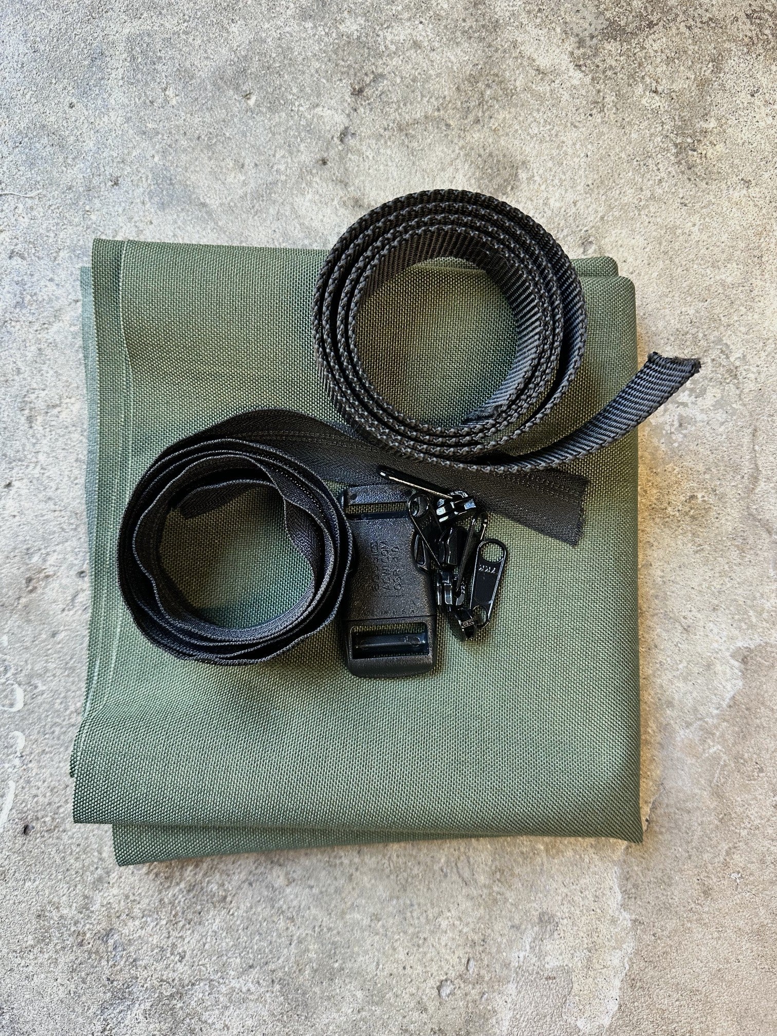 Green fabric with black straps and buckles and zipper pulls on a concrete surface