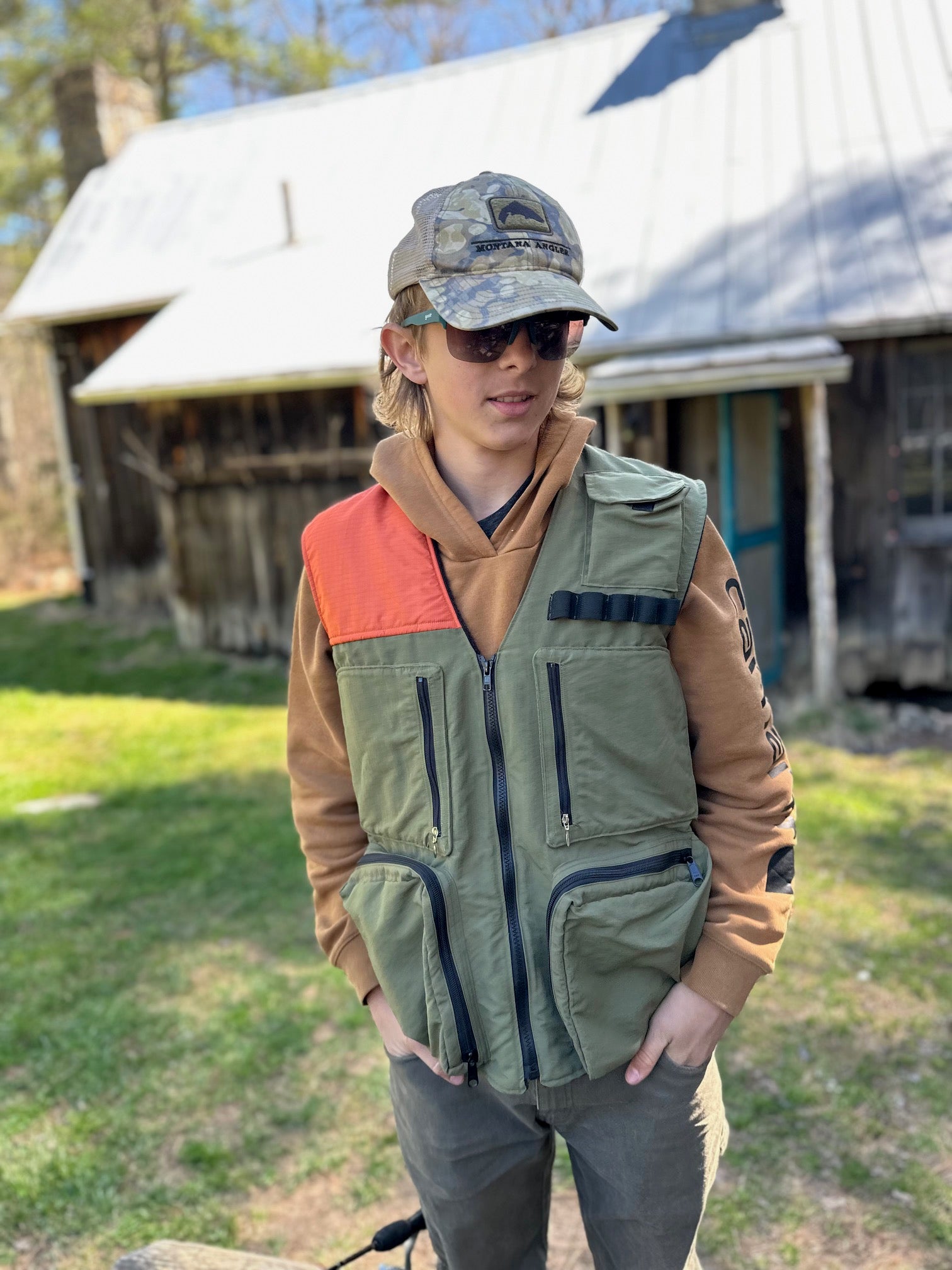 Person wearing a green and orange vest with a cabin in the background
