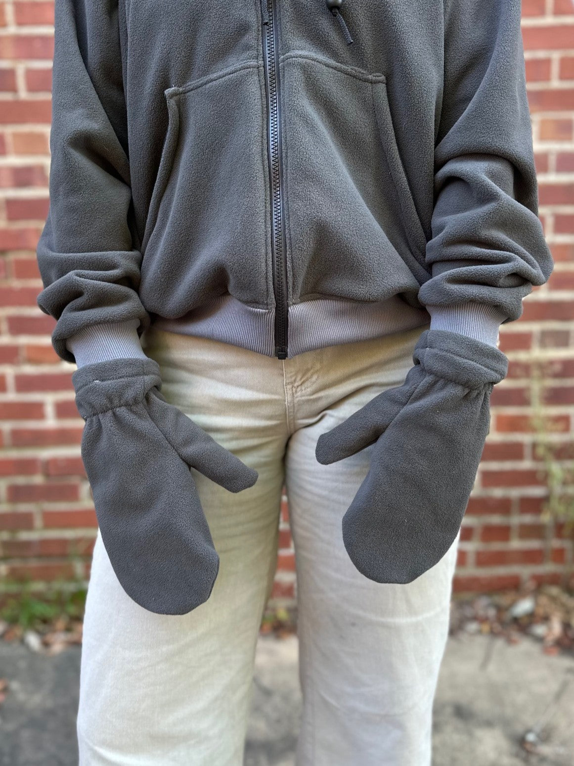 close up of a person with grey fleece mittens, grey sweatshirt, and tan pants