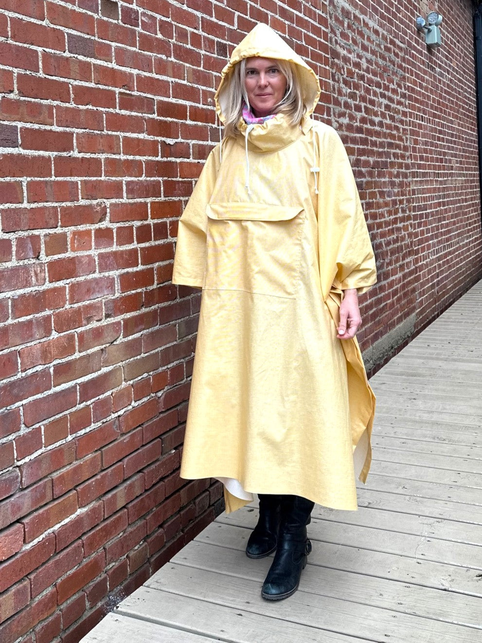 Woman standing in a yellow rain poncho with a hood by a brick wall