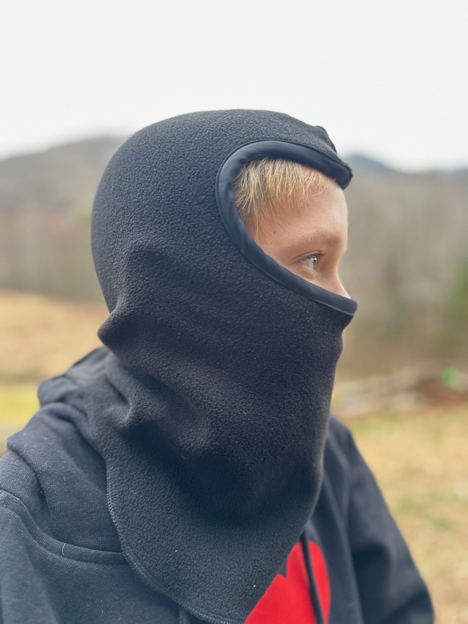 Side view of boy wearing a black fleece balaclava outside