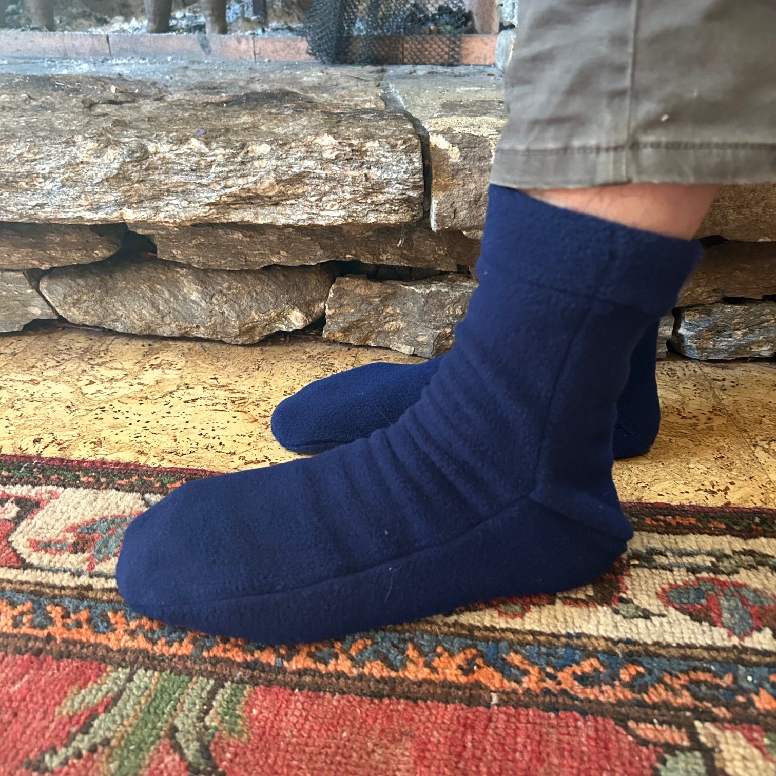 navy blue polar slippers ono feet by a rug and stone hearth