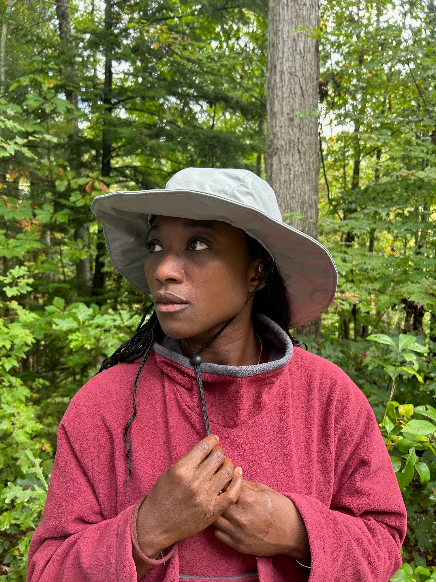Woman wearing a grey hat and red fleece sweater in a fores setting.