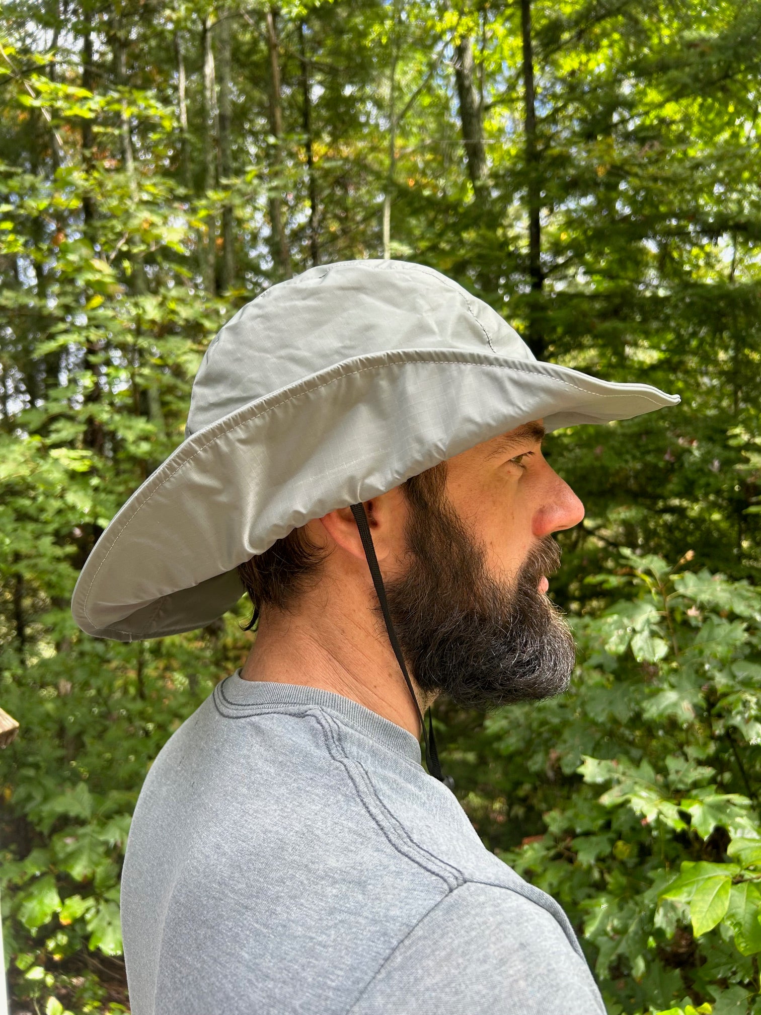Person wearing a wide-brimmed grey  hat outdoors with greenery in the background