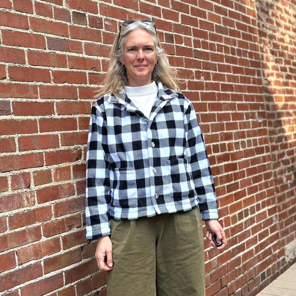 Woman standing in front of a brick wall wearing a black and white buffalo plaid polar lodge jacket.