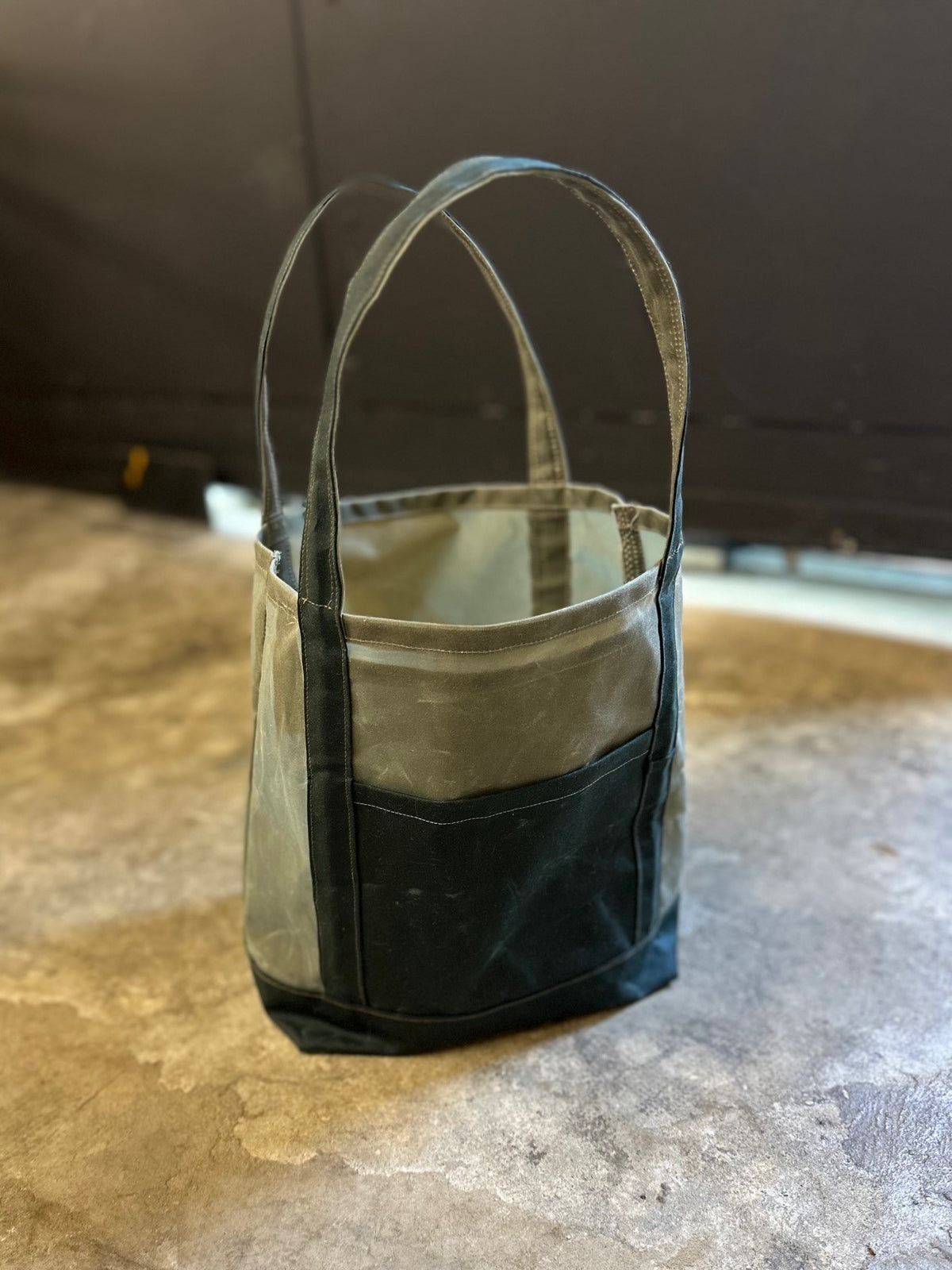 olive green bag with dark green pockets on a concrete floor.