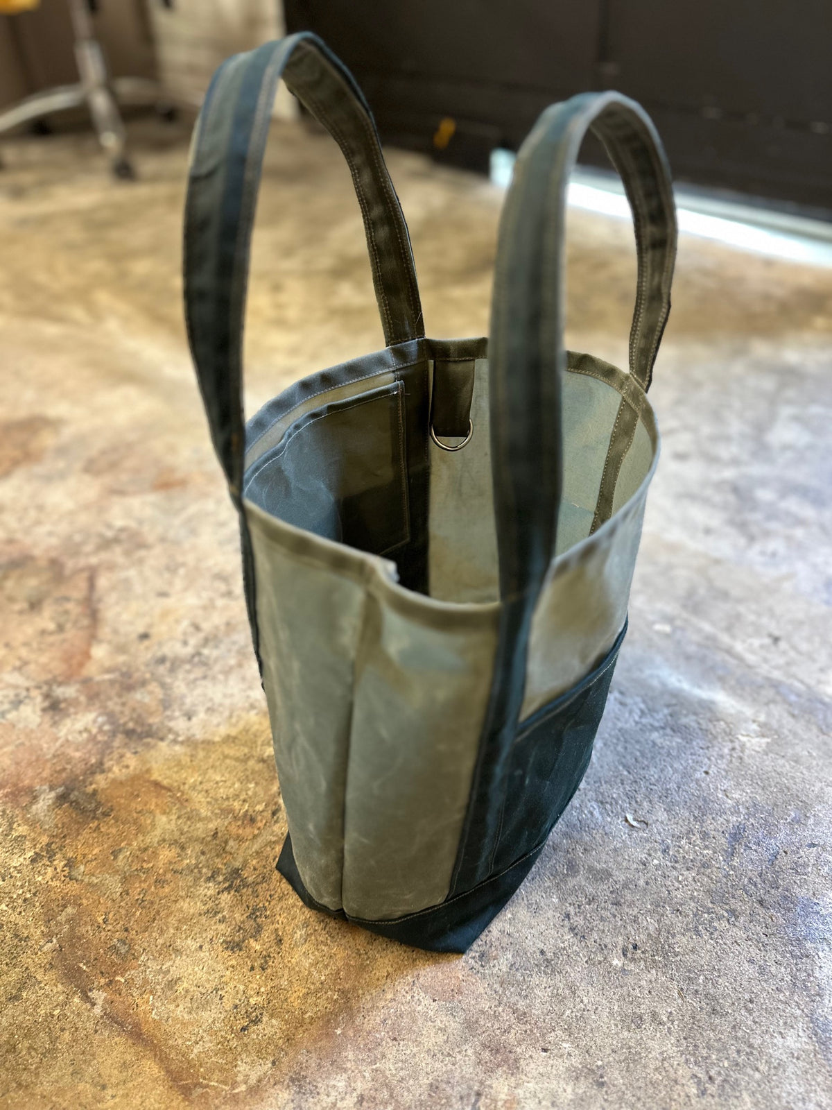 olive green bag with dark green pockets on a concrete floor.