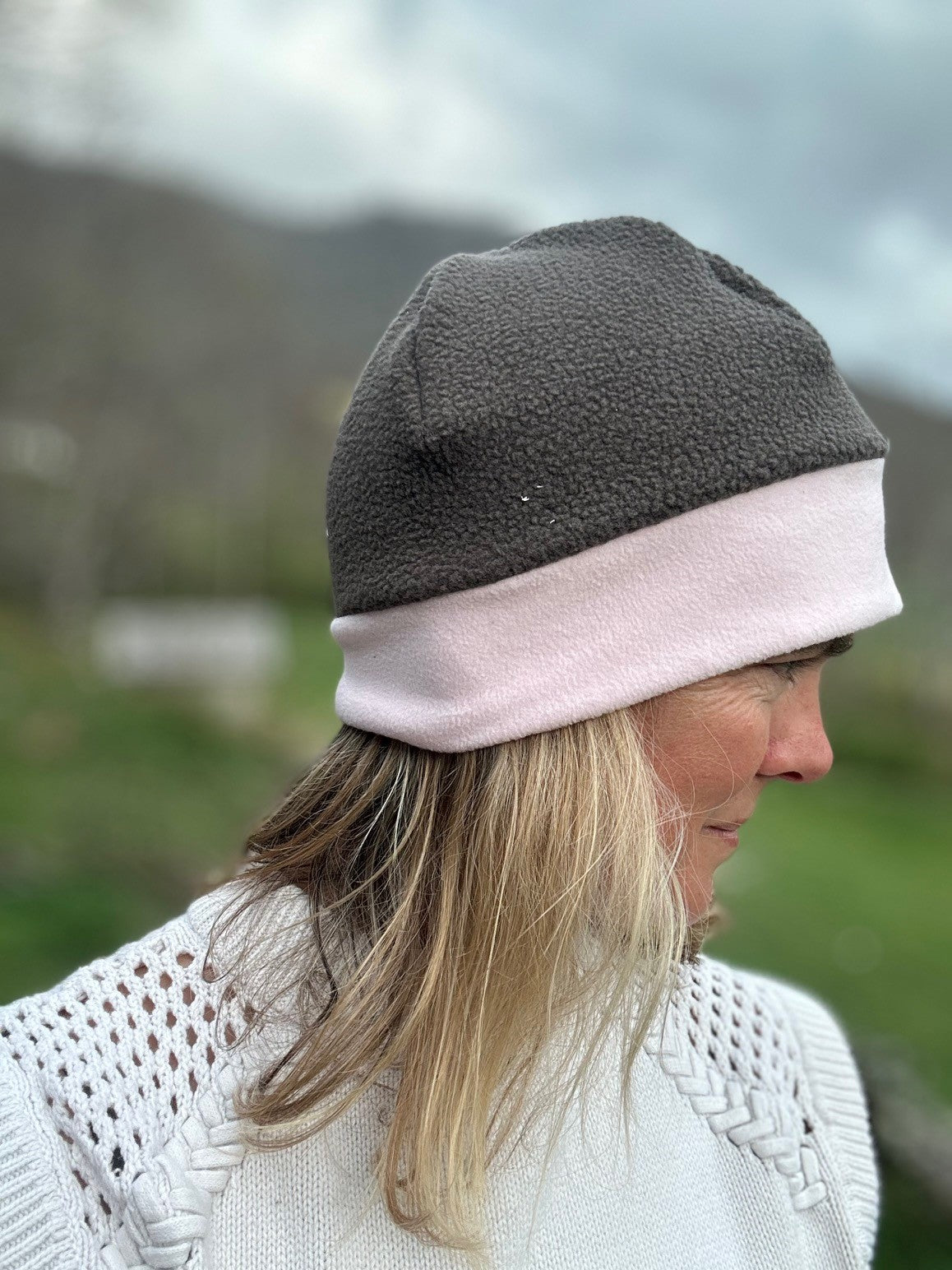 Head shot of woman standing outside wearing a grey and pink border beanie.  Side view
