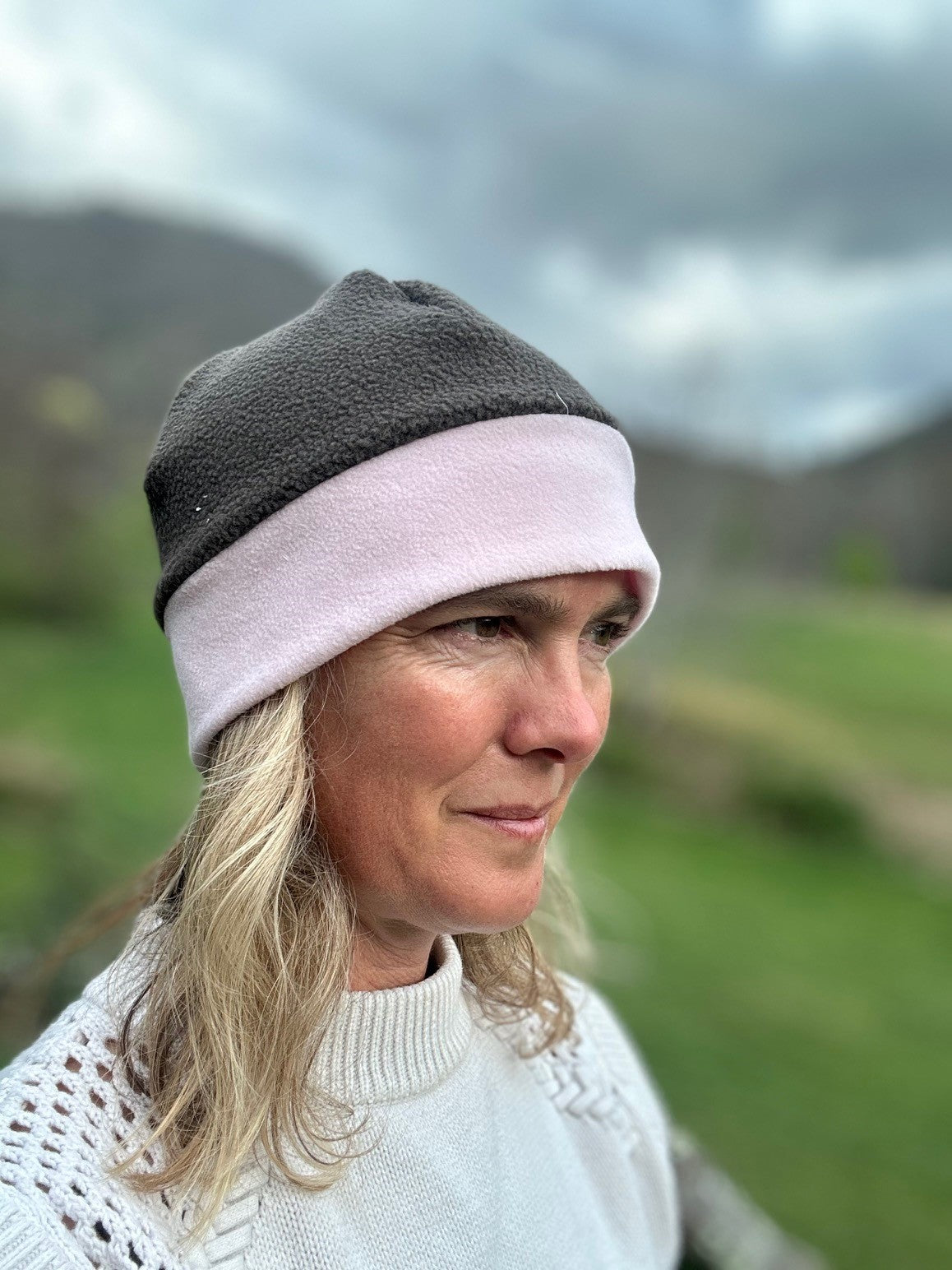 Head shot of woman standing outside wearing a grey and pink border beanie.