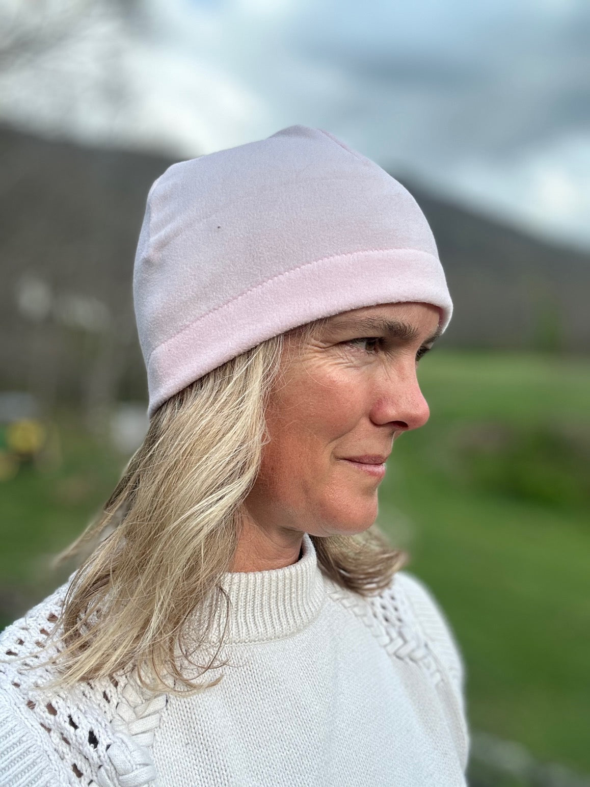 Head shot of woman standing outside wearing a pink beanie. Side View