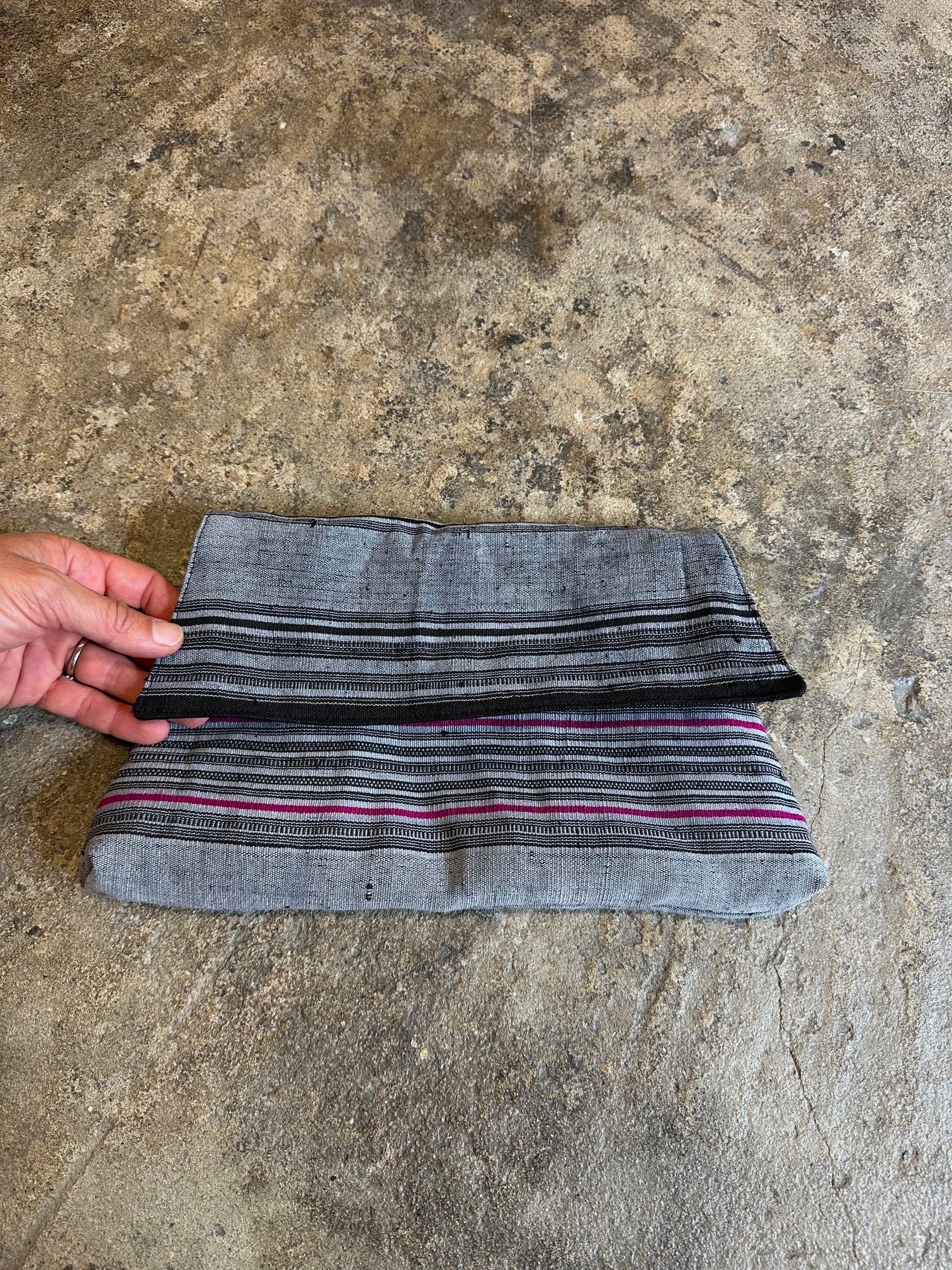fabric clutch with striped pattern held by a hand on a concrete surface