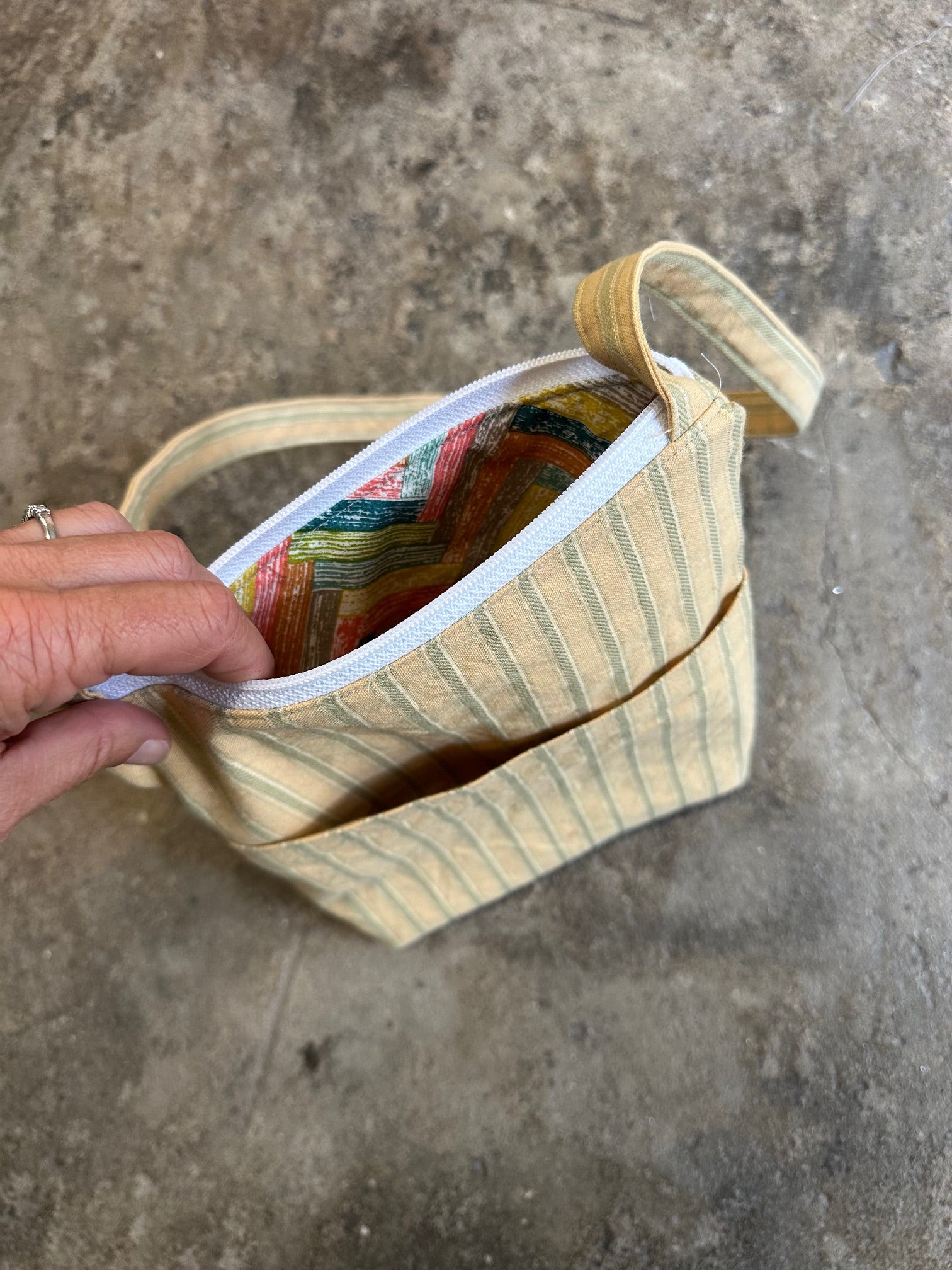 Hand holding a colorful fabric item against a concrete background