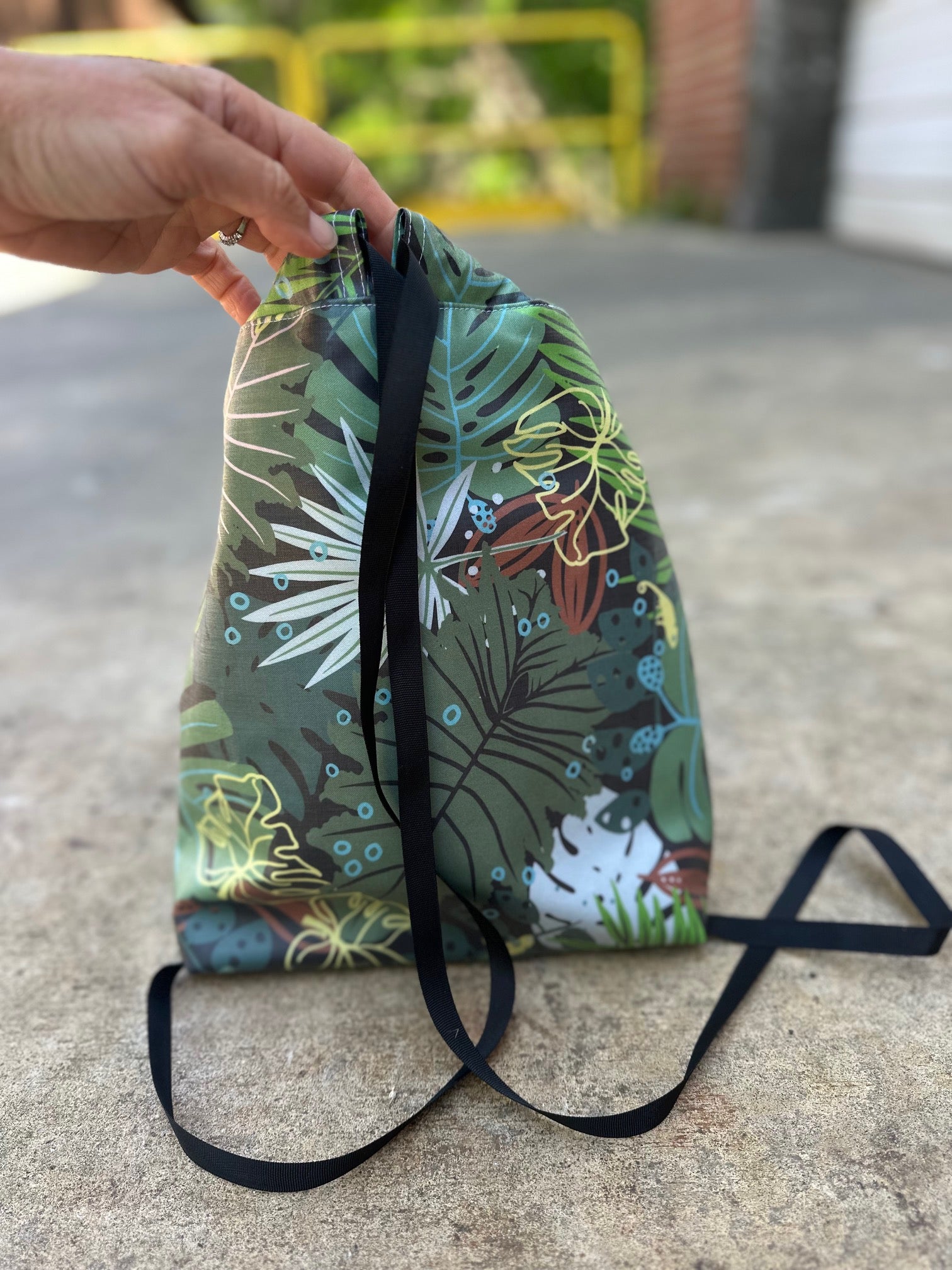 Green drawstring bag with tropical leaf-themed design on a concrete surface