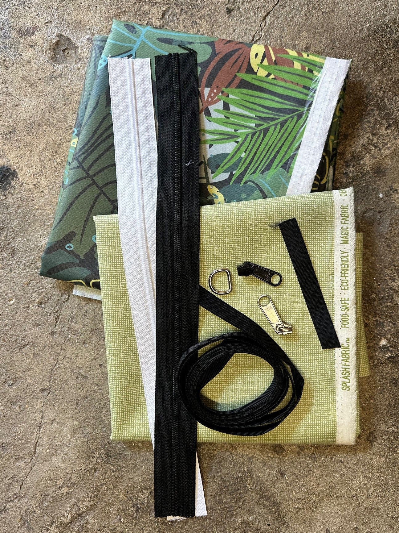 Collection of items including a black zipper, white zipper, zipper pulls, and green fabric on a textured surface.