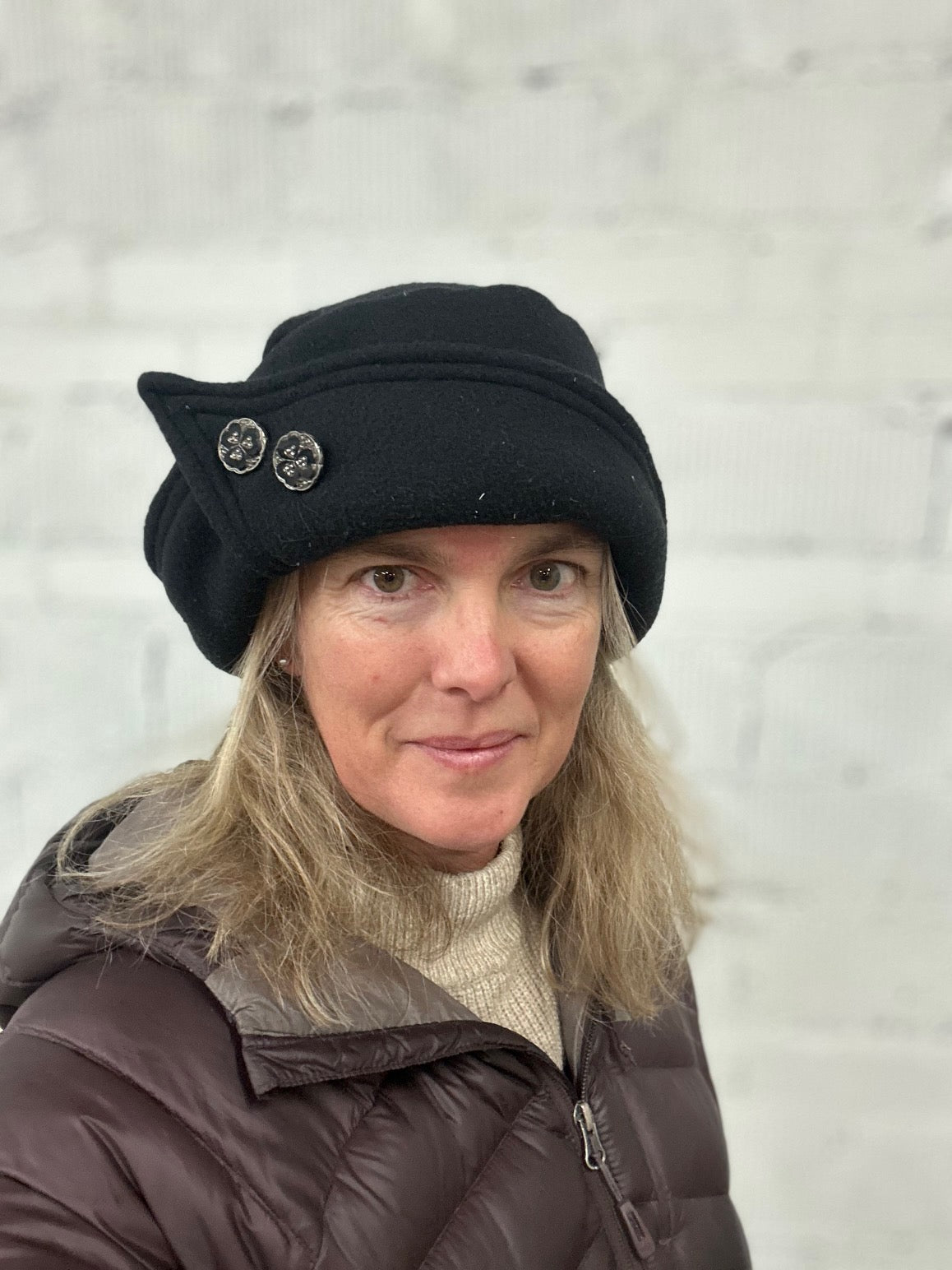 Woman wearing a black roll brim hat with two buttons on it.